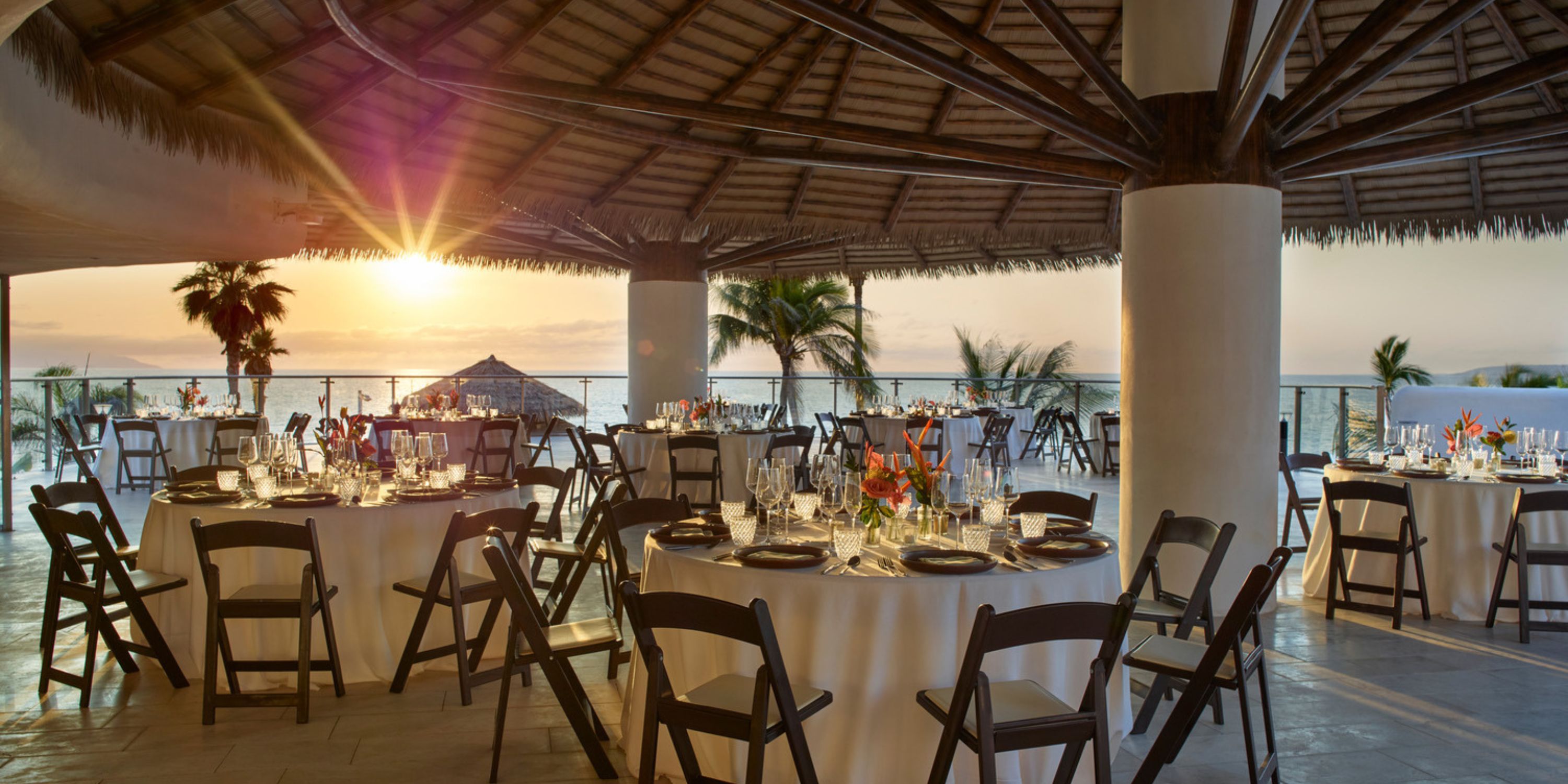 Round tables arranged for a destination wedding under a thatched roof at UNICO 20°105° Riviera Nayarit.