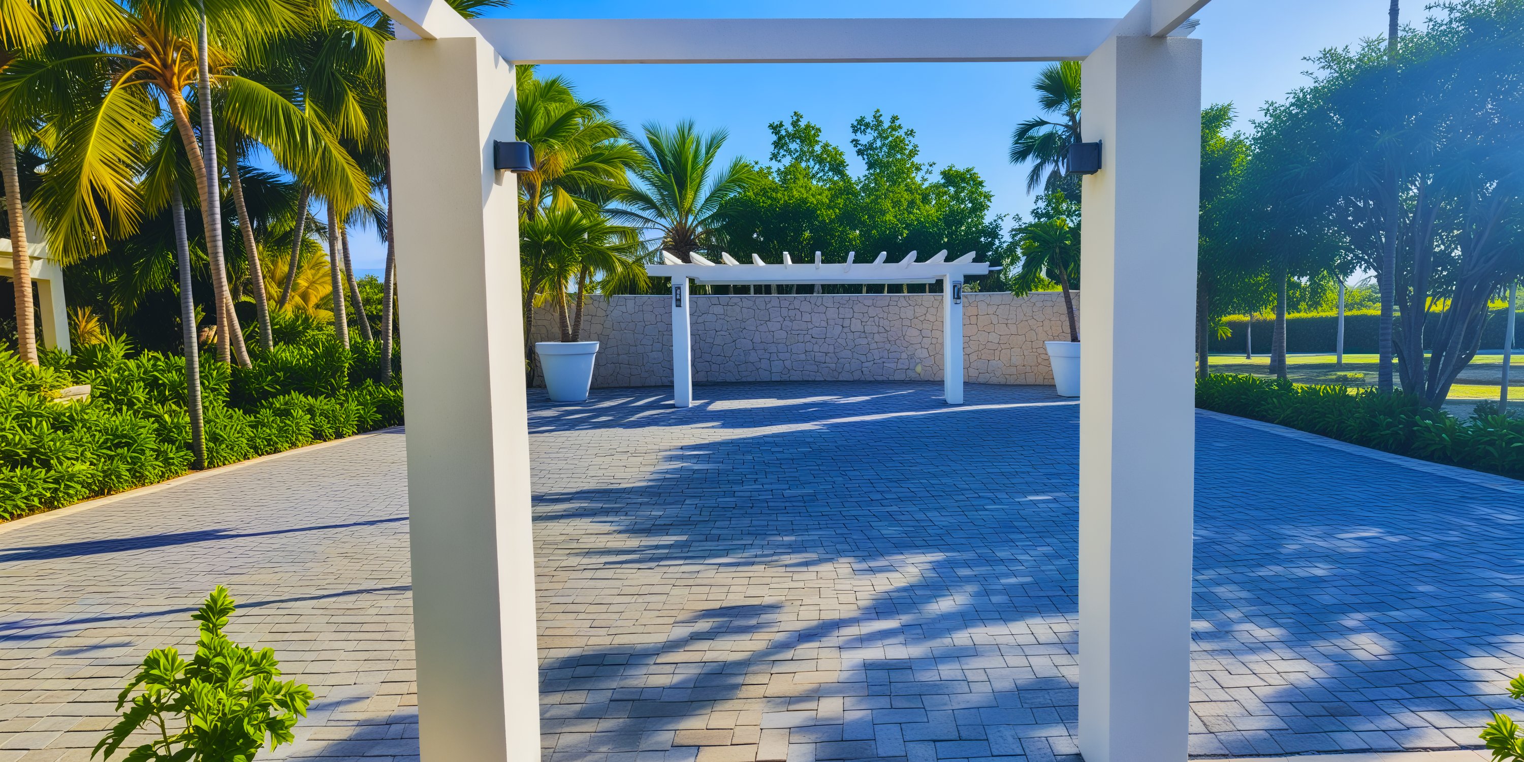 A stunning brick driveway lined with palm trees leads the way to a destination wedding, featuring a charming pergola under a clear blue sky.