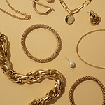 On a beige surface lay an array of exquisite jewelry perfect for a destination wedding: gleaming gold necklaces, elegant bracelets, sophisticated earrings, and a lustrous pearl stud.