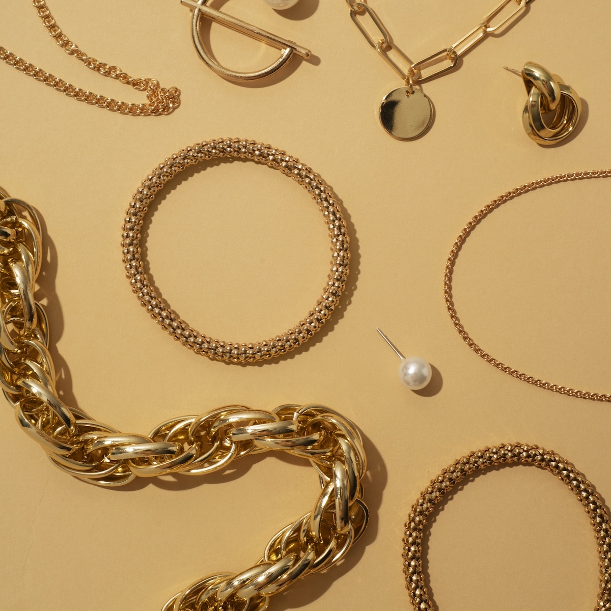 On a beige surface lay an array of exquisite jewelry perfect for a destination wedding: gleaming gold necklaces, elegant bracelets, sophisticated earrings, and a lustrous pearl stud.