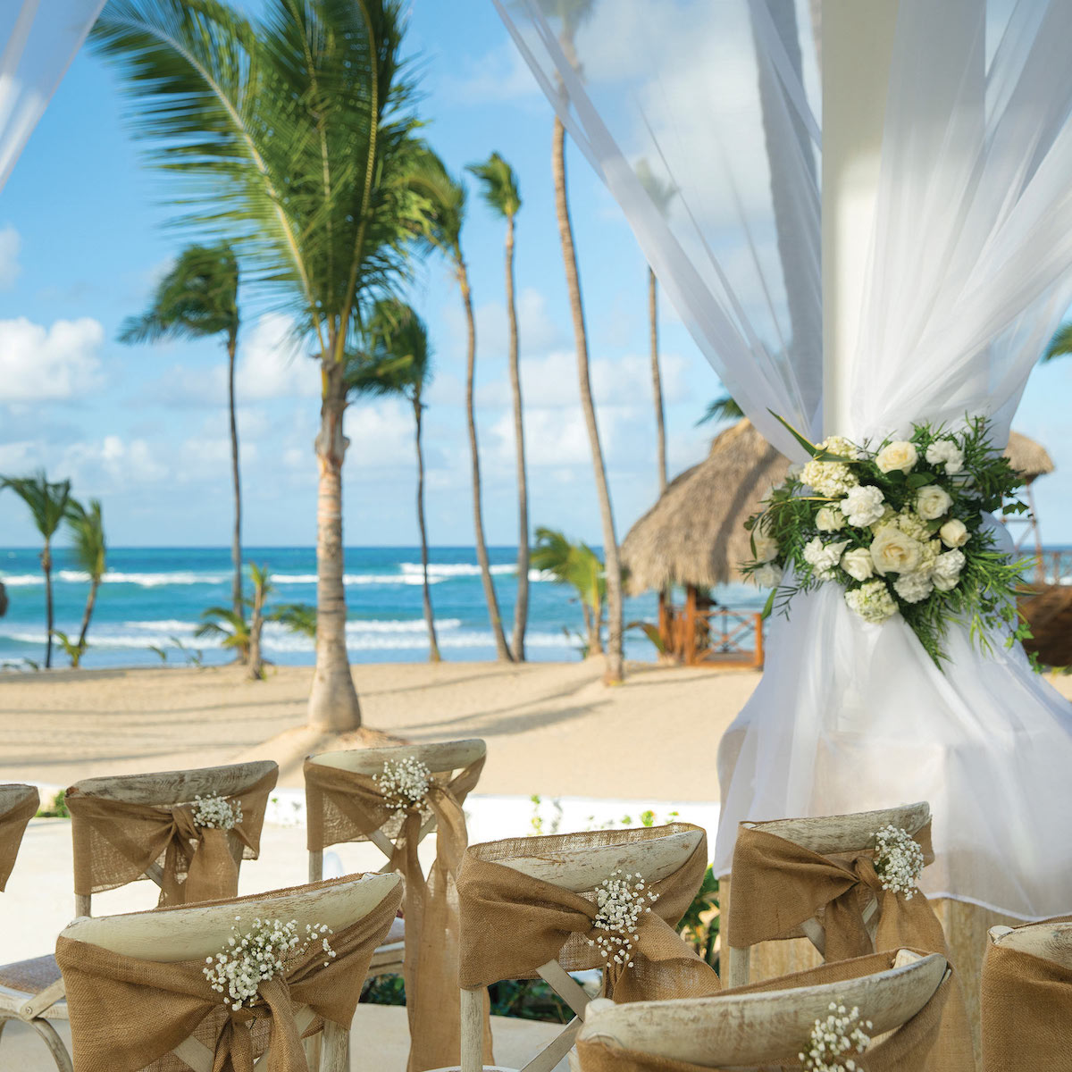 A picturesque beachfront arrangement perfect for a destination wedding, complete with elegantly arranged chairs and beautiful floral decorations.