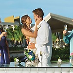 The bride and groom are beaming alongside their friends, all holding champagne glasses at the outdoor wedding celebration.