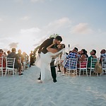 Aubrey and Noah share a kiss at the altar during their destination wedding on a sandy beach, surrounded by guests as the sun sets.