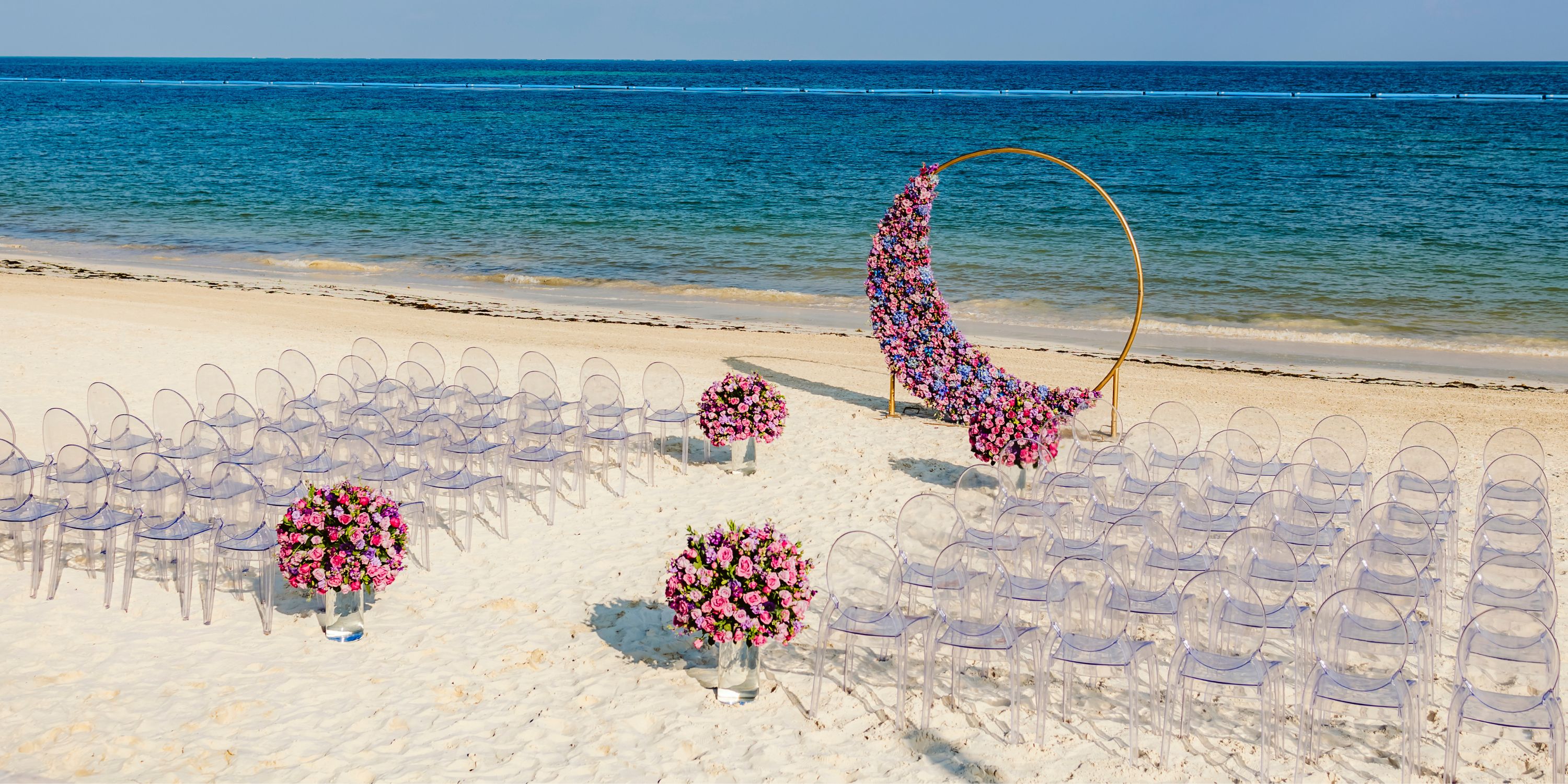 Clear chairs and pink flowers decorate a destination wedding by the sea at Moon Palace Nizuc.