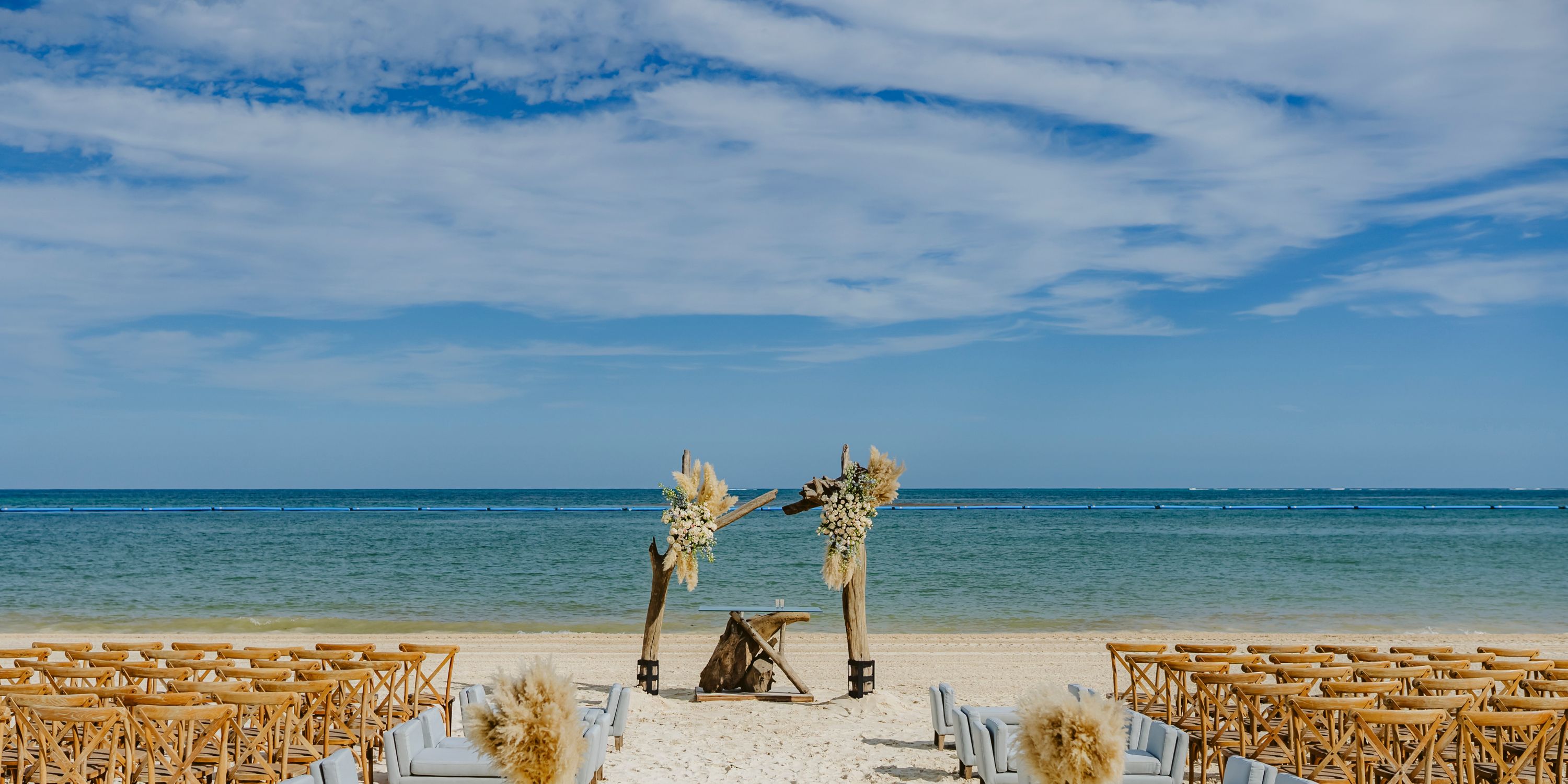 Destination wedding on the beach at Moon Palace Nizuc, featuring wooden chairs and a floral arch by the ocean.