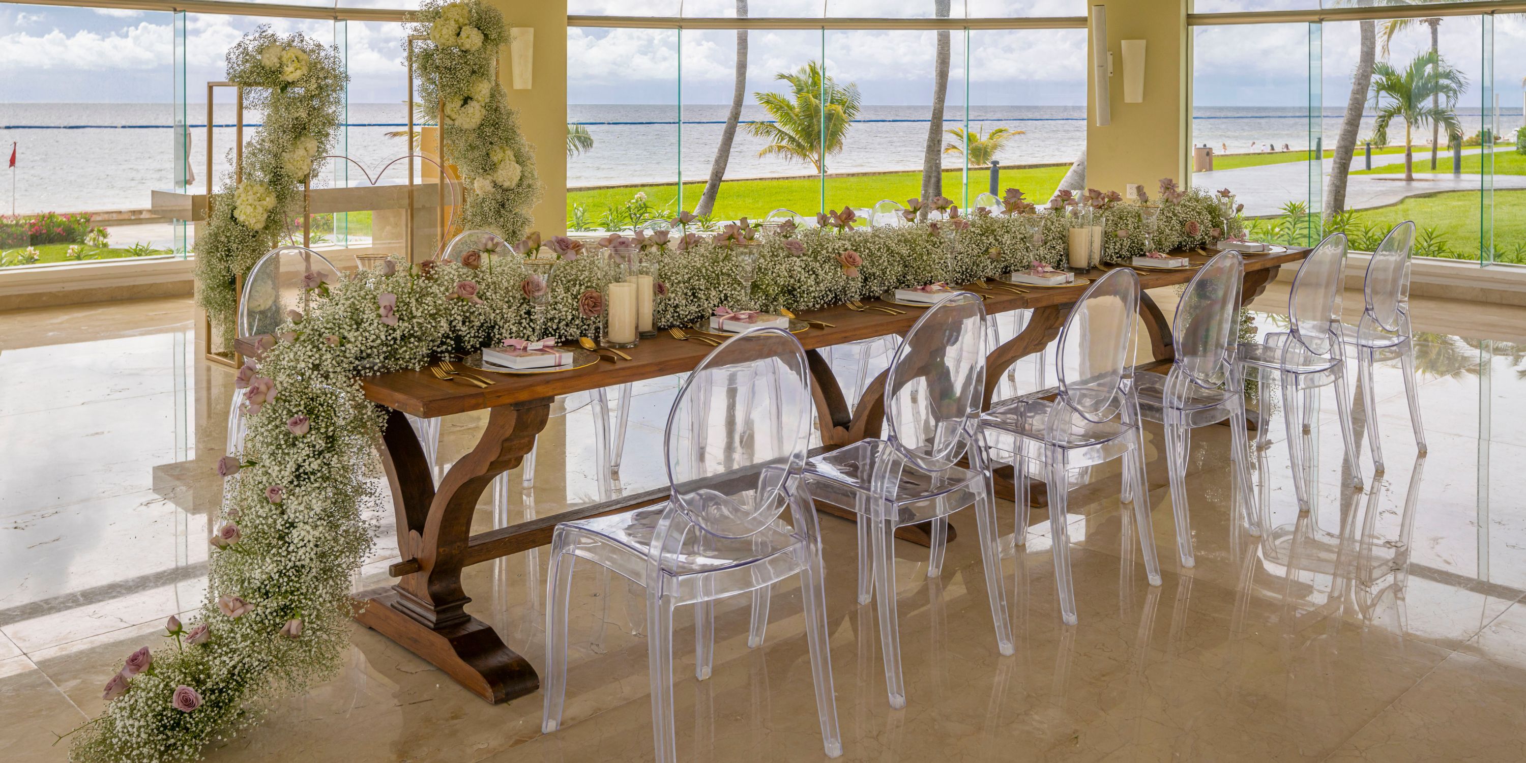 Elegant long wooden wedding table with florals and clear chairs at Moon Palace Nizuc by water views.