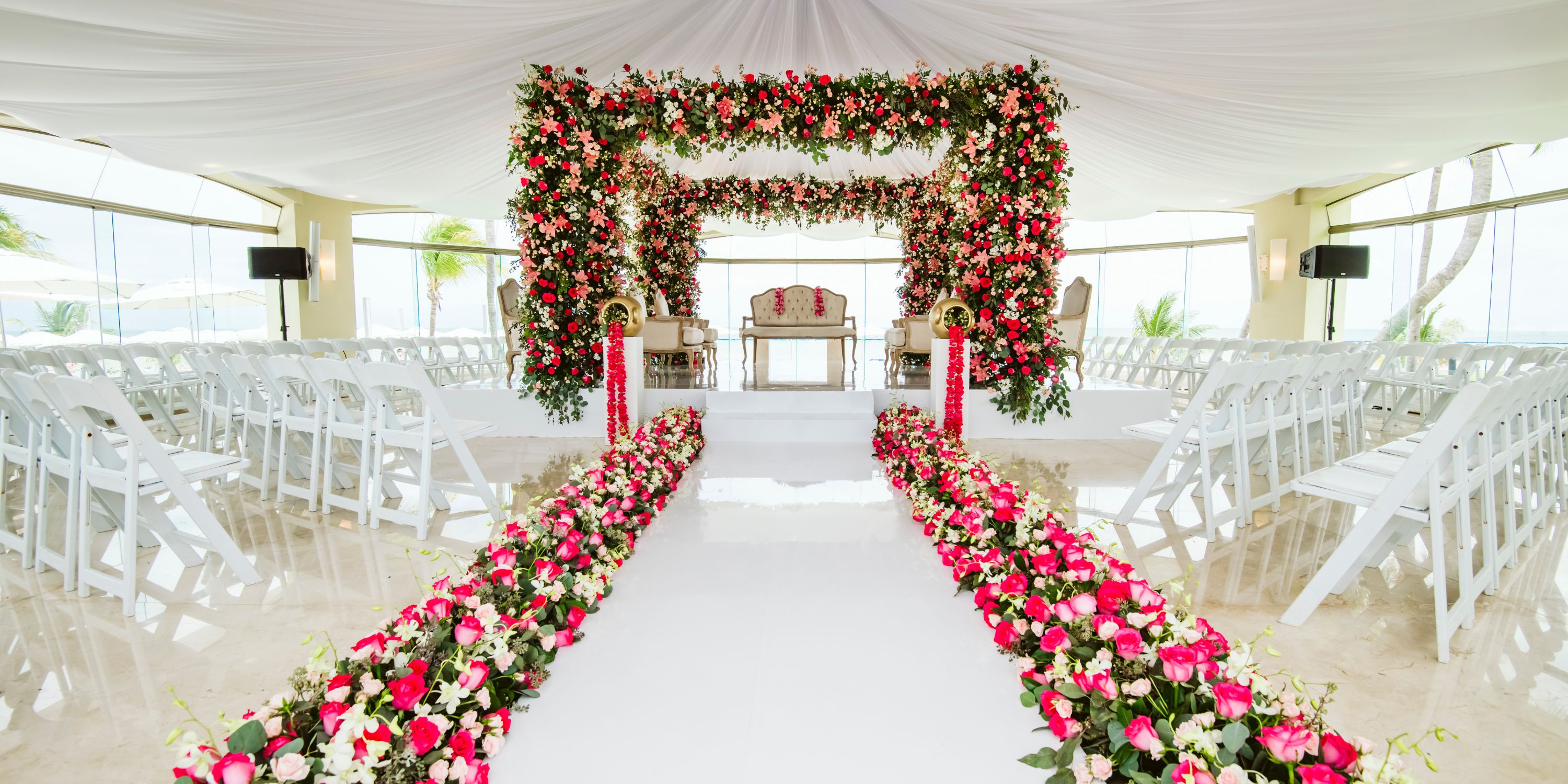 Elegant destination wedding at Moon Palace Nizuc: indoor floral arch, white chairs, pink flower aisle.