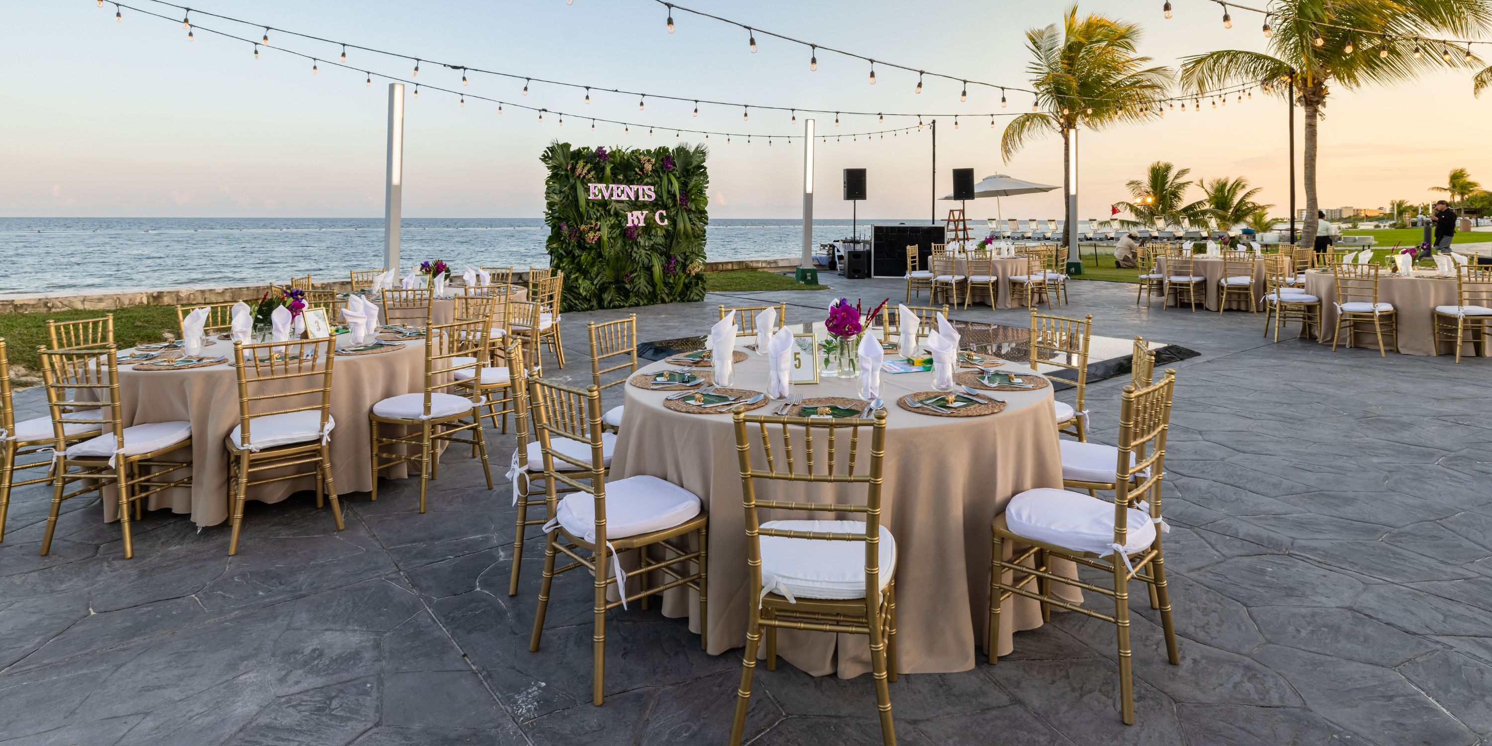 Destination wedding setup at Moon Palace Nizuc: round tables, gold chairs, and string lights at sunset.