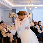 At their wedding reception, the bride and groom share an intimate embrace on the dance floor as guests look on from nearby tables.