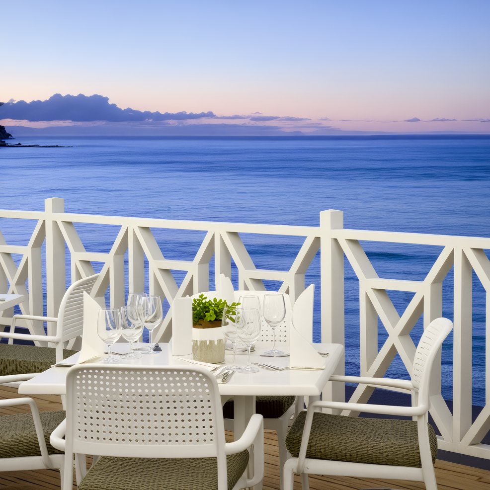 Outdoor dining table with wedding glassware on a balcony, overlooking the ocean at sunset for a destination wedding.