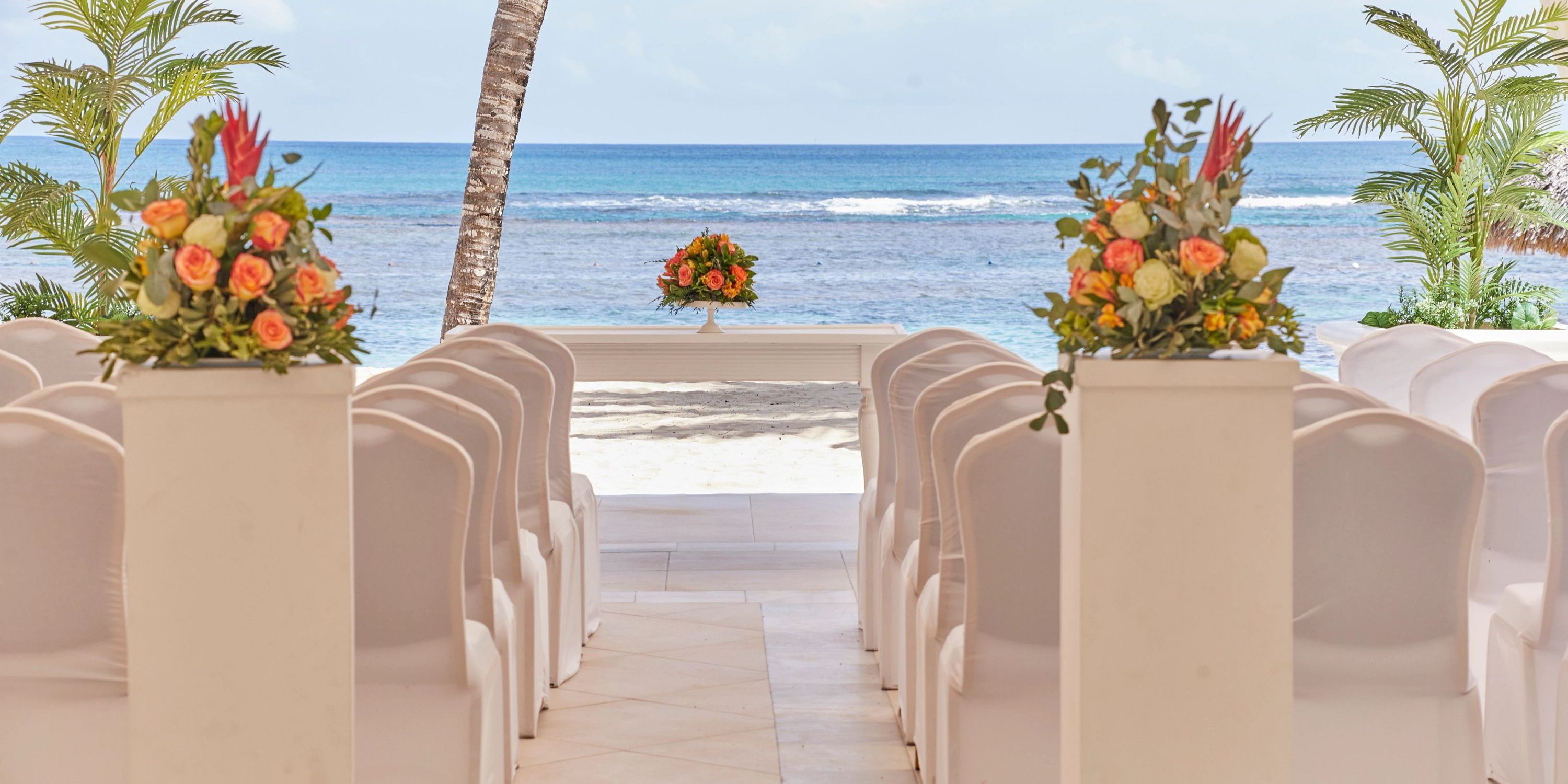White chairs line up before a floral table at a destination wedding on the beach at Bahia Principe Grand El Portillo.