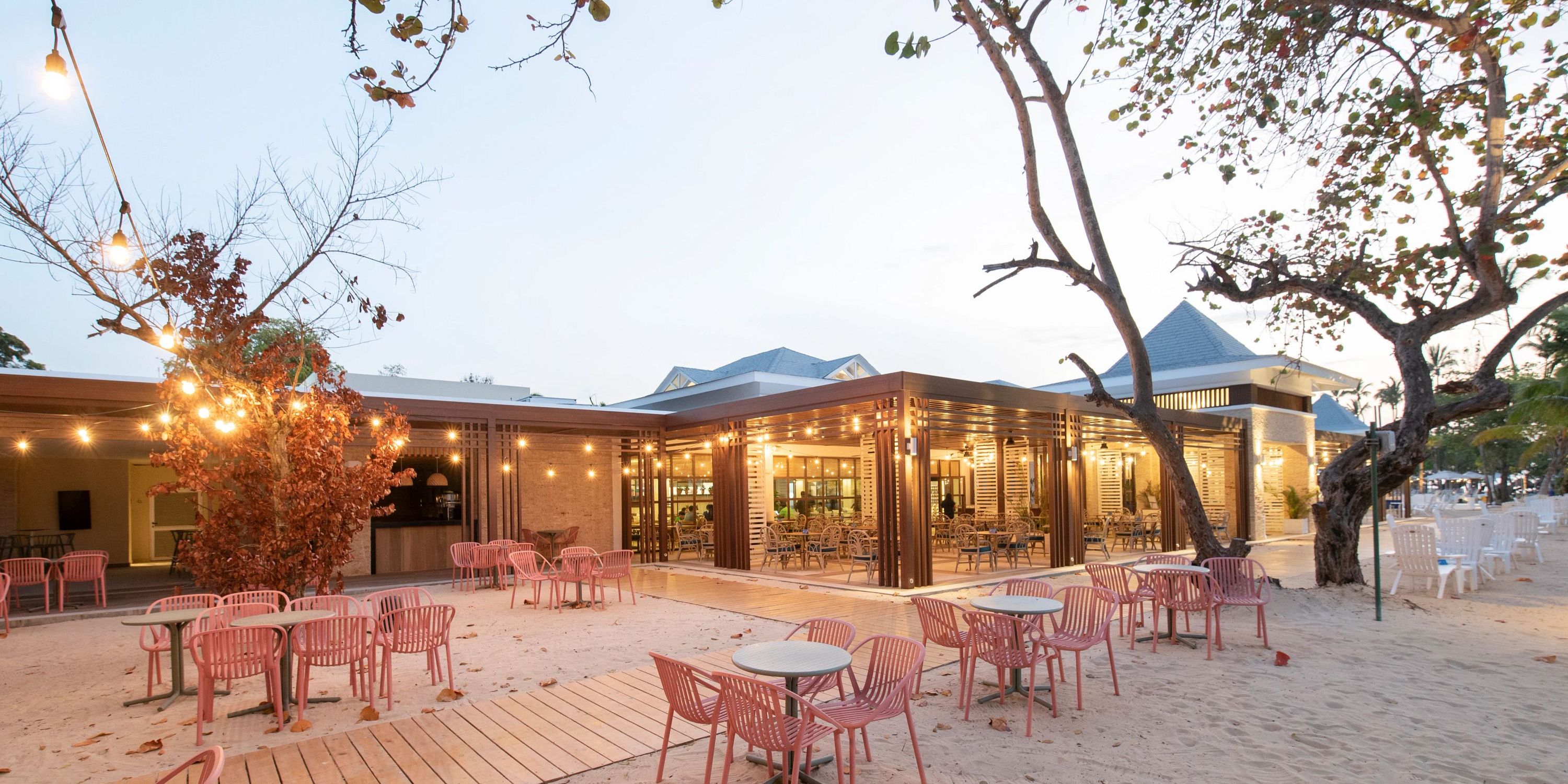 Bahia Principe Grand El Portillo’s beachside restaurant set for a destination wedding at sunset, with pink chairs and string lights.