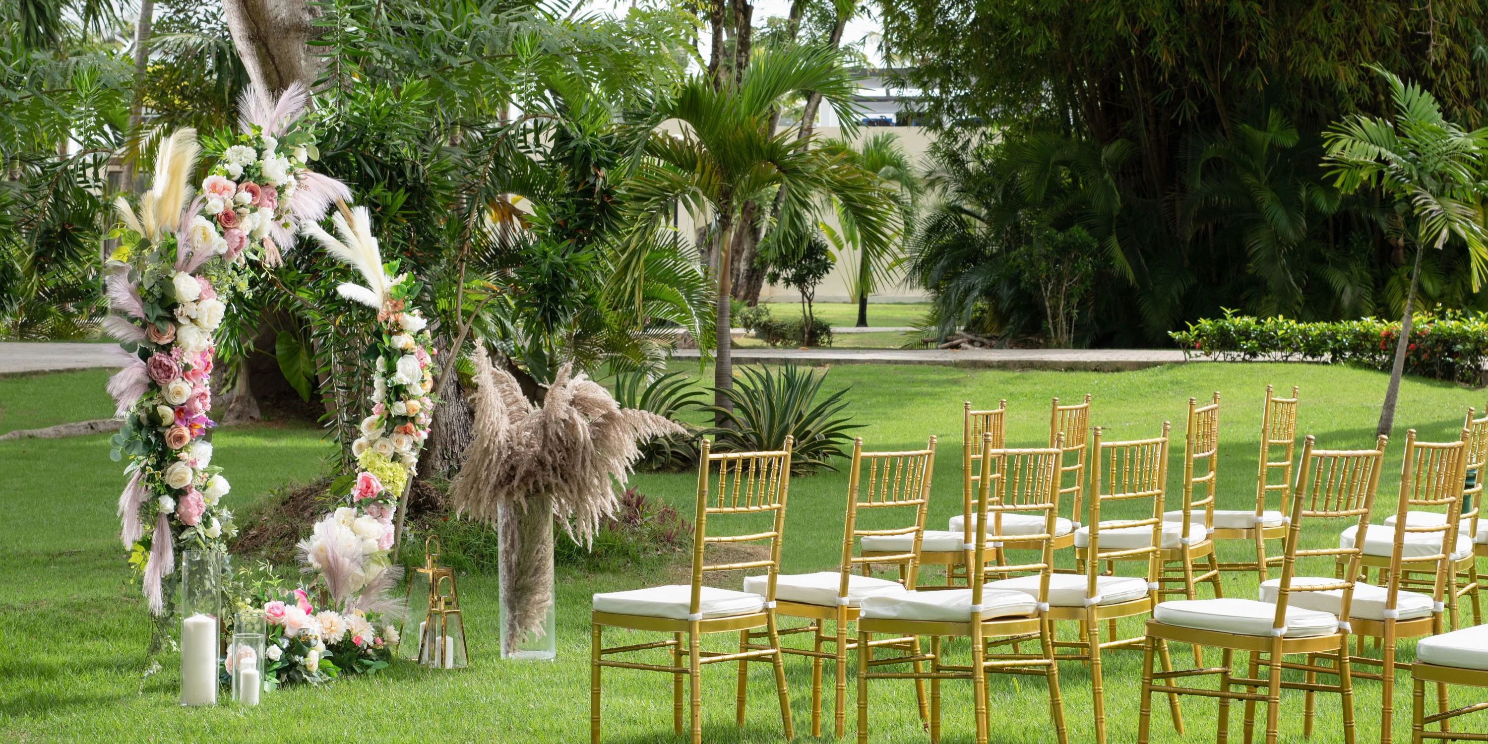 Gold chairs are arranged for a destination wedding on the lawn, facing a floral arch at El Portillo.