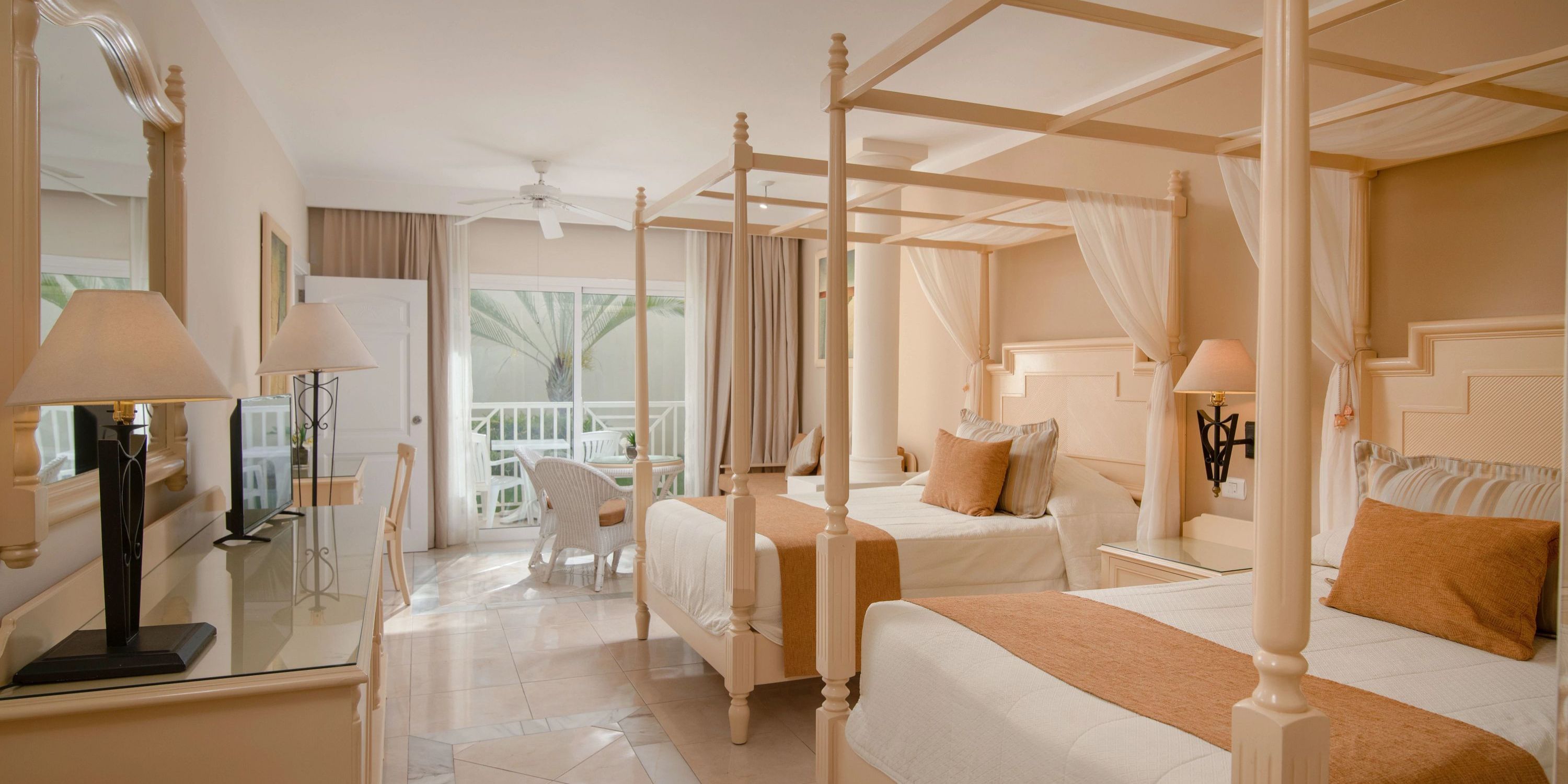 Bahia Principe Grand El Portillo wedding suite: 2 canopy beds, desk, TV, lamps, balcony seating.