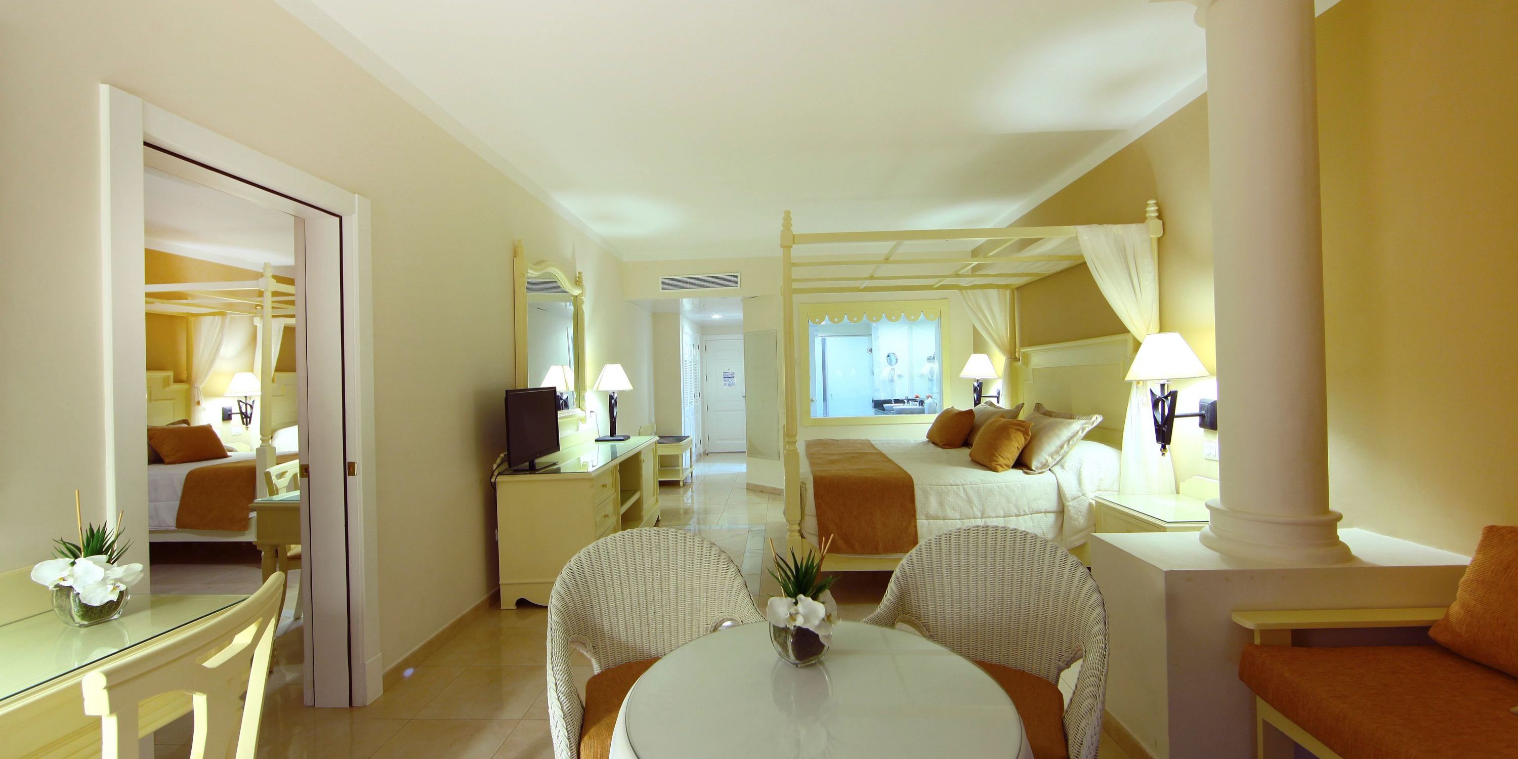 Elegant room at Bahia Principe Grand El Portillo, perfect for a destination wedding, features canopy bed, TV, mirrors, and ambient lighting.