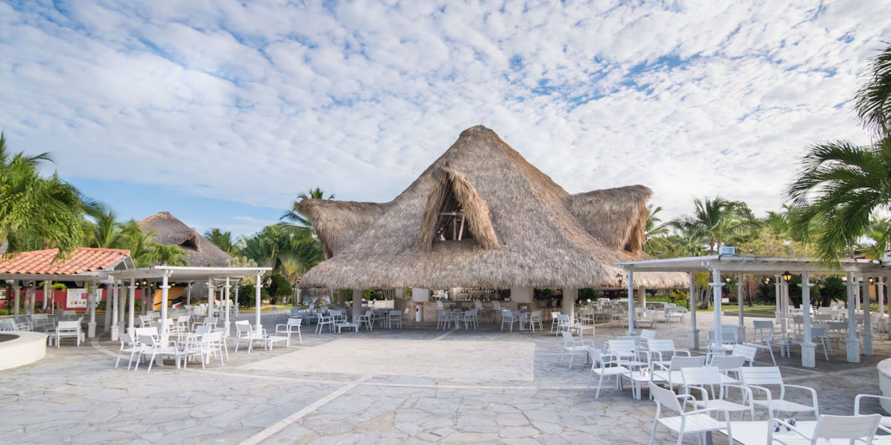Catalonia Bayahibe: open-air restaurant with thatched roof, palm trees, white chairs—ideal for a destination wedding.