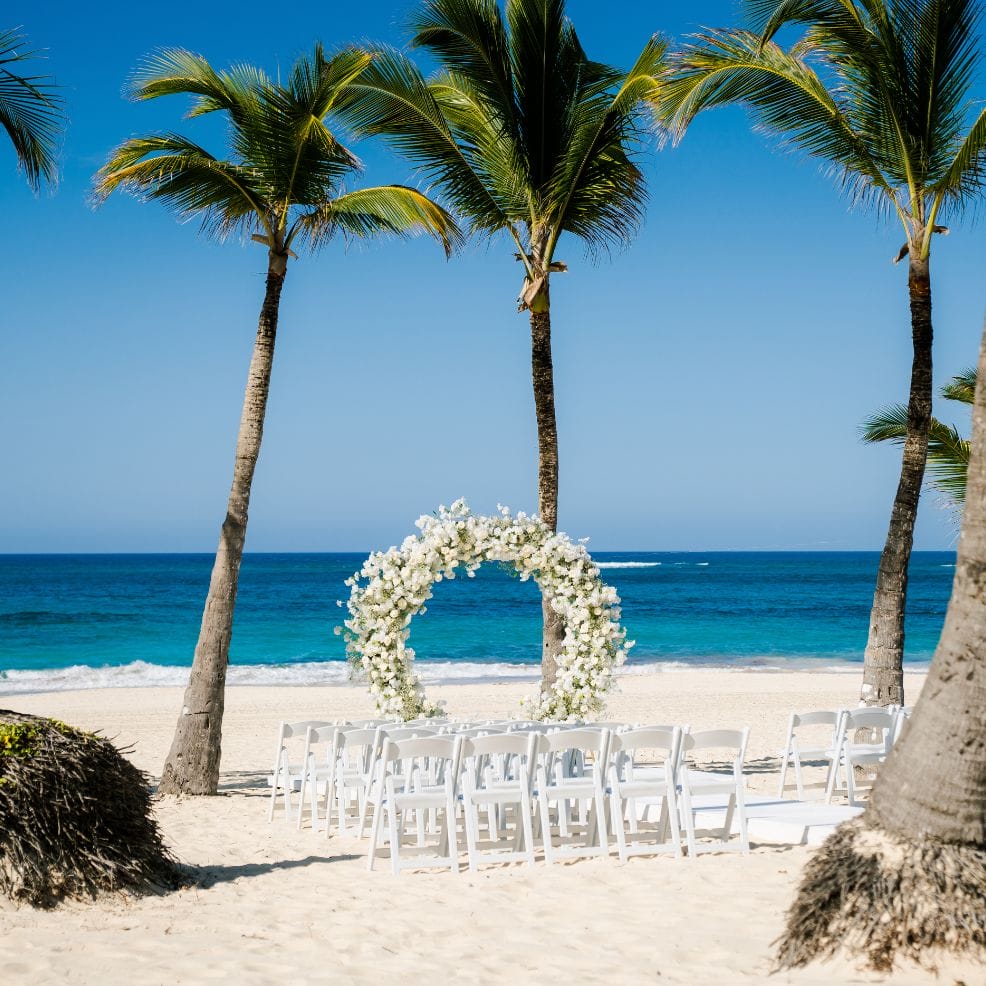 White chairs and a floral arch create a beautiful destination wedding setup beneath swaying palm trees.