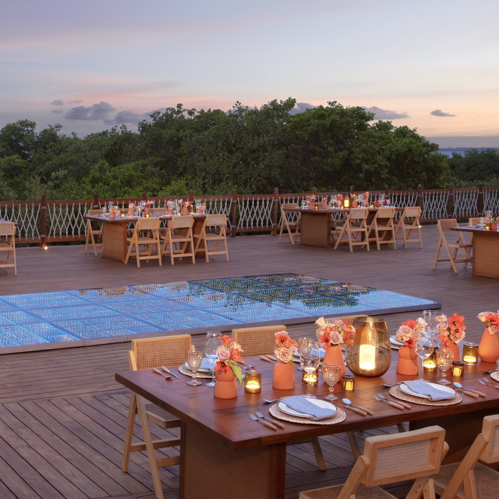 Elegant wedding dining setup with candlelit, decorated tables by a covered pool at sunset—perfect for a destination wedding.