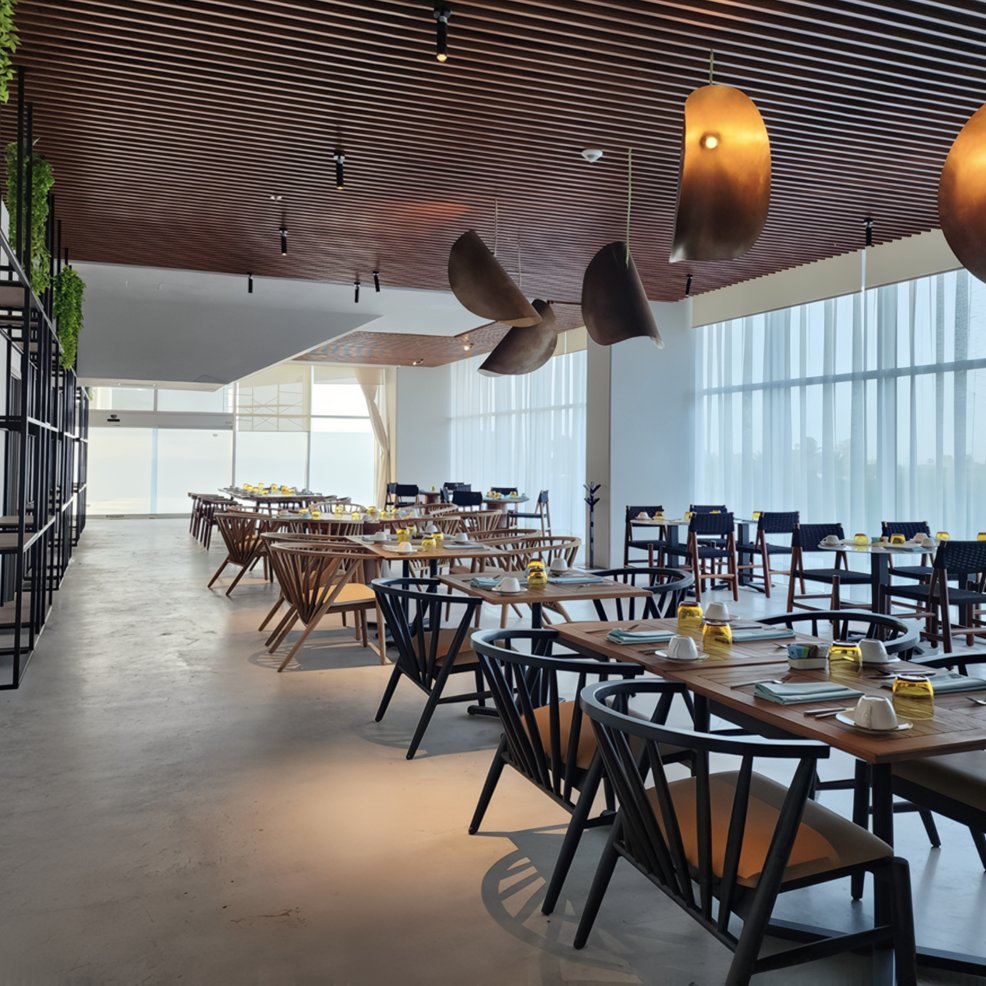 Modern restaurant set for a destination wedding, with wooden tables, black chairs, and bright windows.
