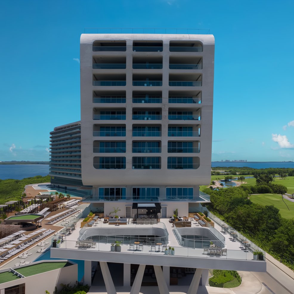 Elegant modern hotel with balconies, ideal for destination weddings, framed by pools, greenery, and sky.
