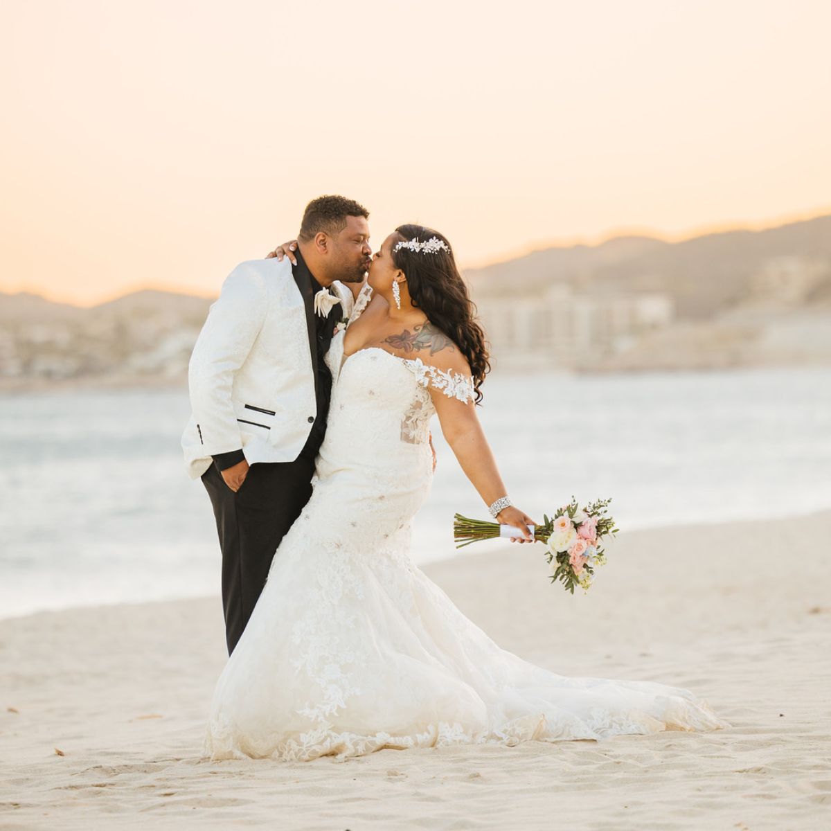Tiffany and Anthony at their destination wedding, posing on a sunset beach as the bride holds her bouquet.