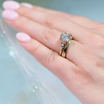 A hand with soft pink nails displays a gold diamond ring set, perfect for a dreamy destination wedding.