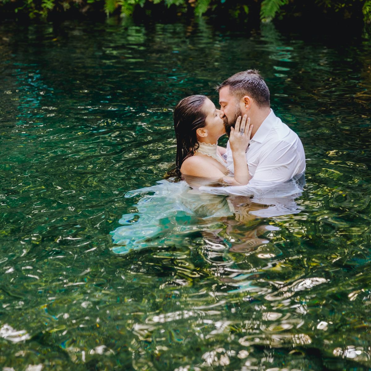 Kathryn and Mike share a kiss in formal wedding attire, standing in clear water at their destination wedding.