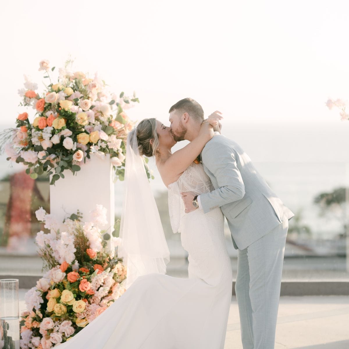 Lauren and Ben (Copy) share a kiss at their destination wedding, surrounded by blooming flowers outdoors.
