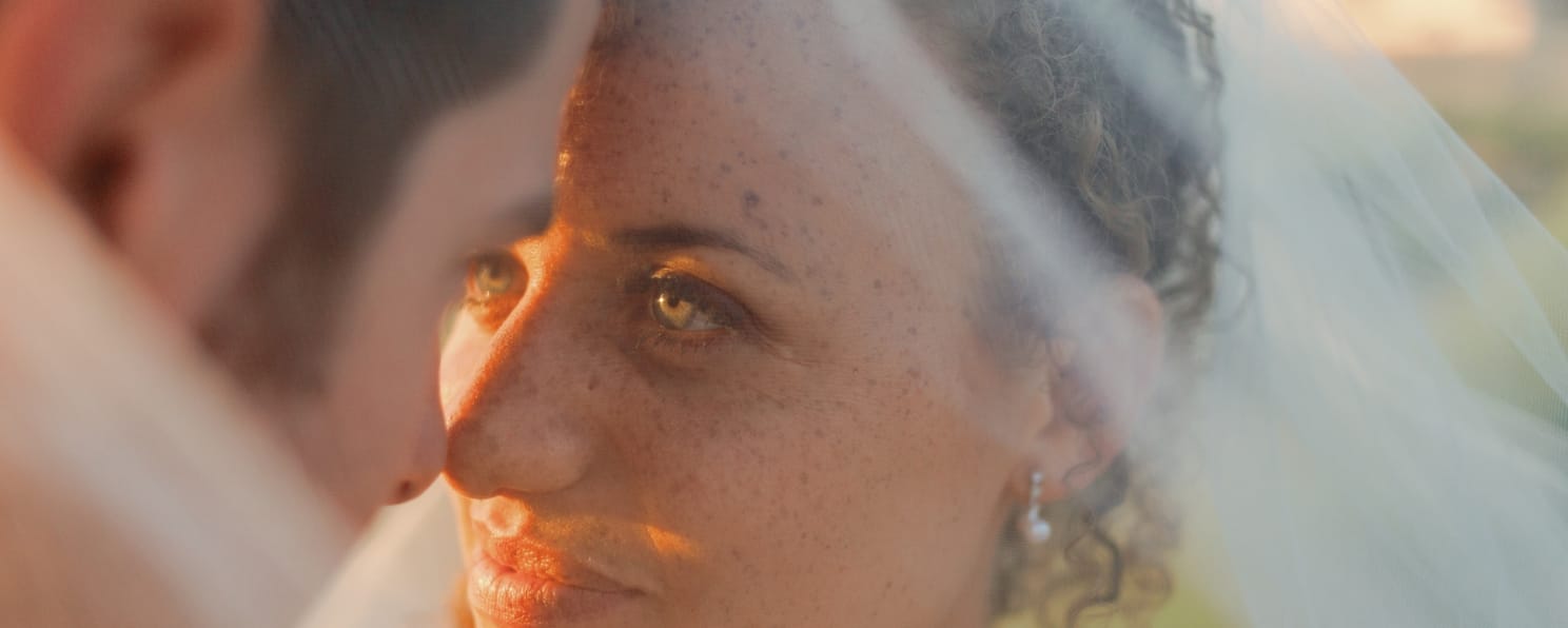 Close-up of a couple at their destination wedding, sunlight illuminating the bride’s face and veil.