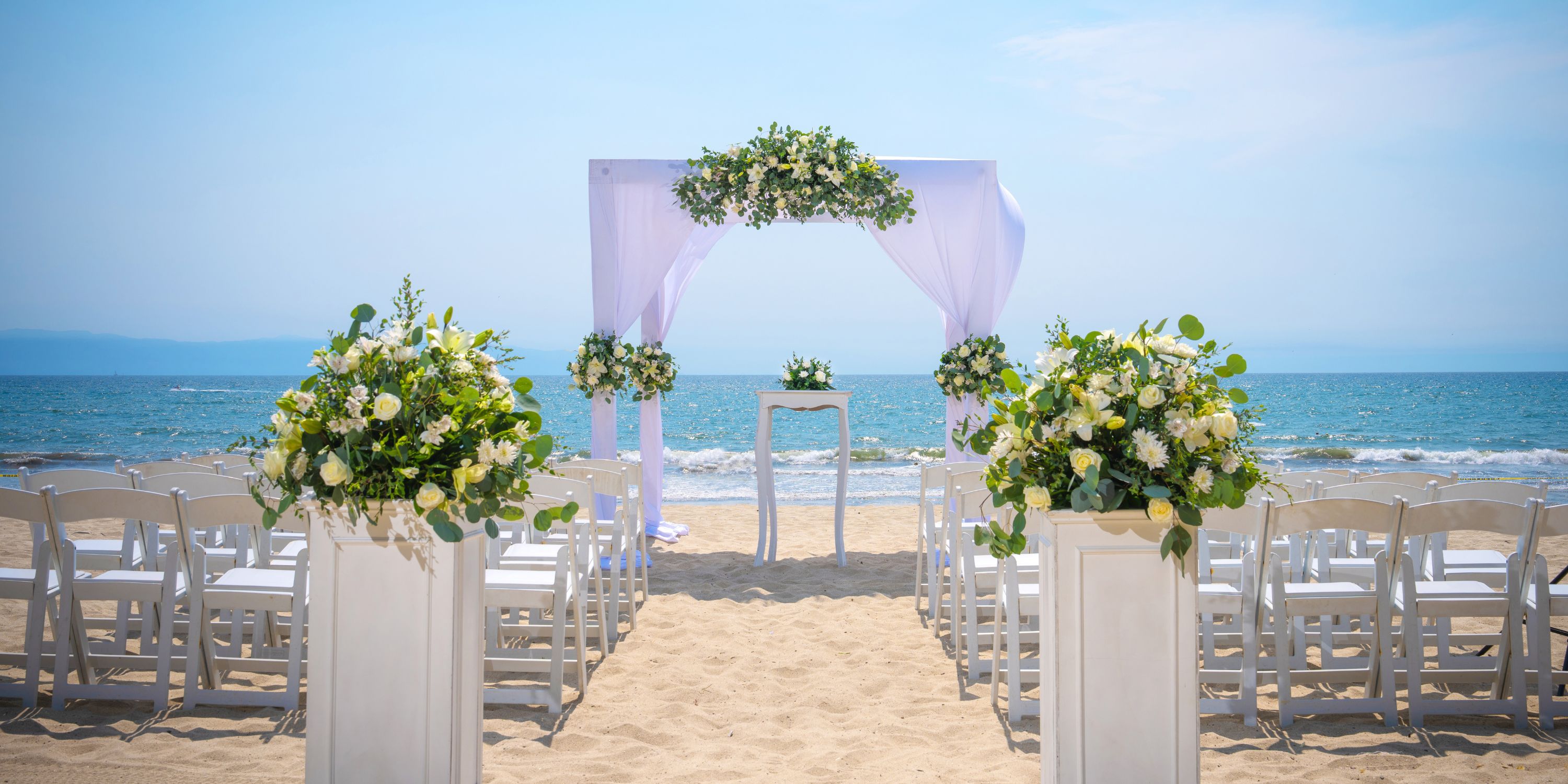 Destination wedding setup at Hotel Riu Jalisco featuring white chairs, flowers, and an arch facing the ocean.