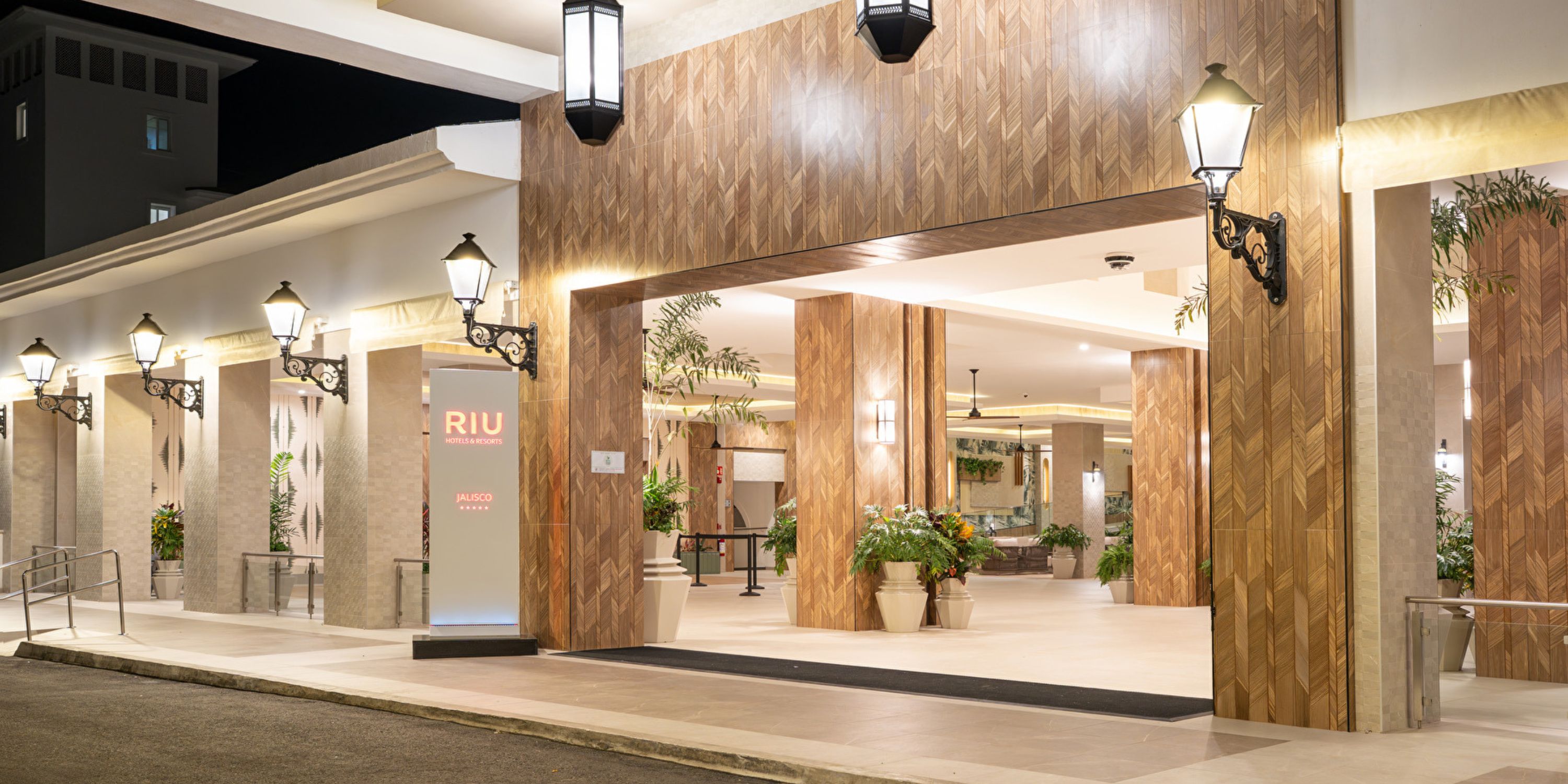 Hotel Riu Jalisco entrance at night, perfect for a destination wedding, with columns, plants, and lamps.