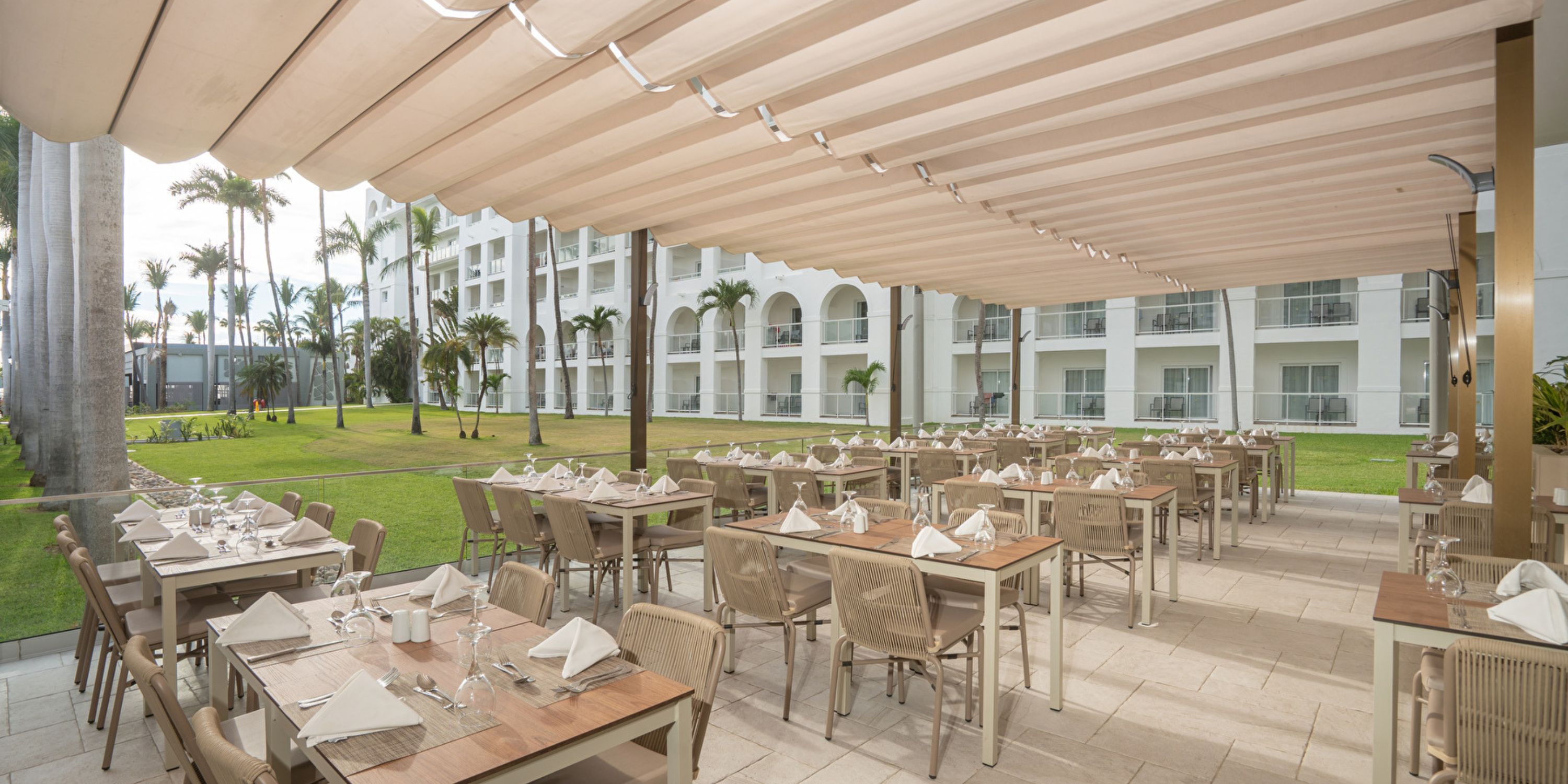 Outdoor dining setup for a destination wedding at Hotel Riu Jalisco, tables under a pergola by the lawn.