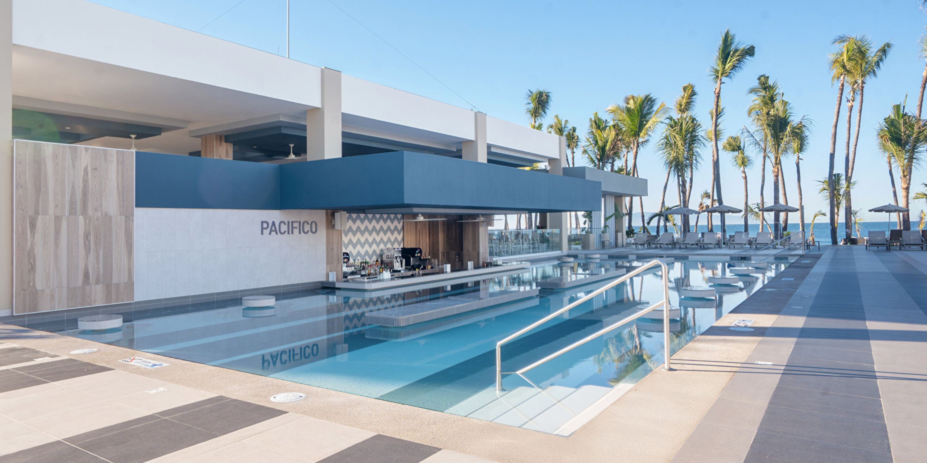 Hotel Riu Jalisco: poolside bar with modern seating, palm trees, ocean views—ideal for a destination wedding.