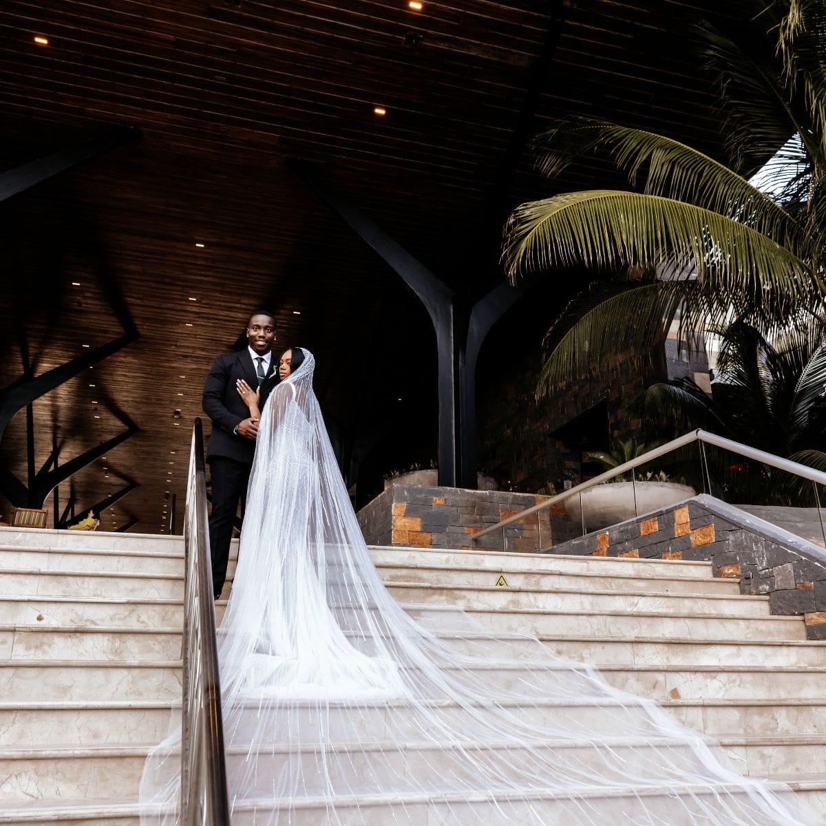 Quishona and Delon (Copy) stand together on stairs at their destination wedding, bride in white veil.
