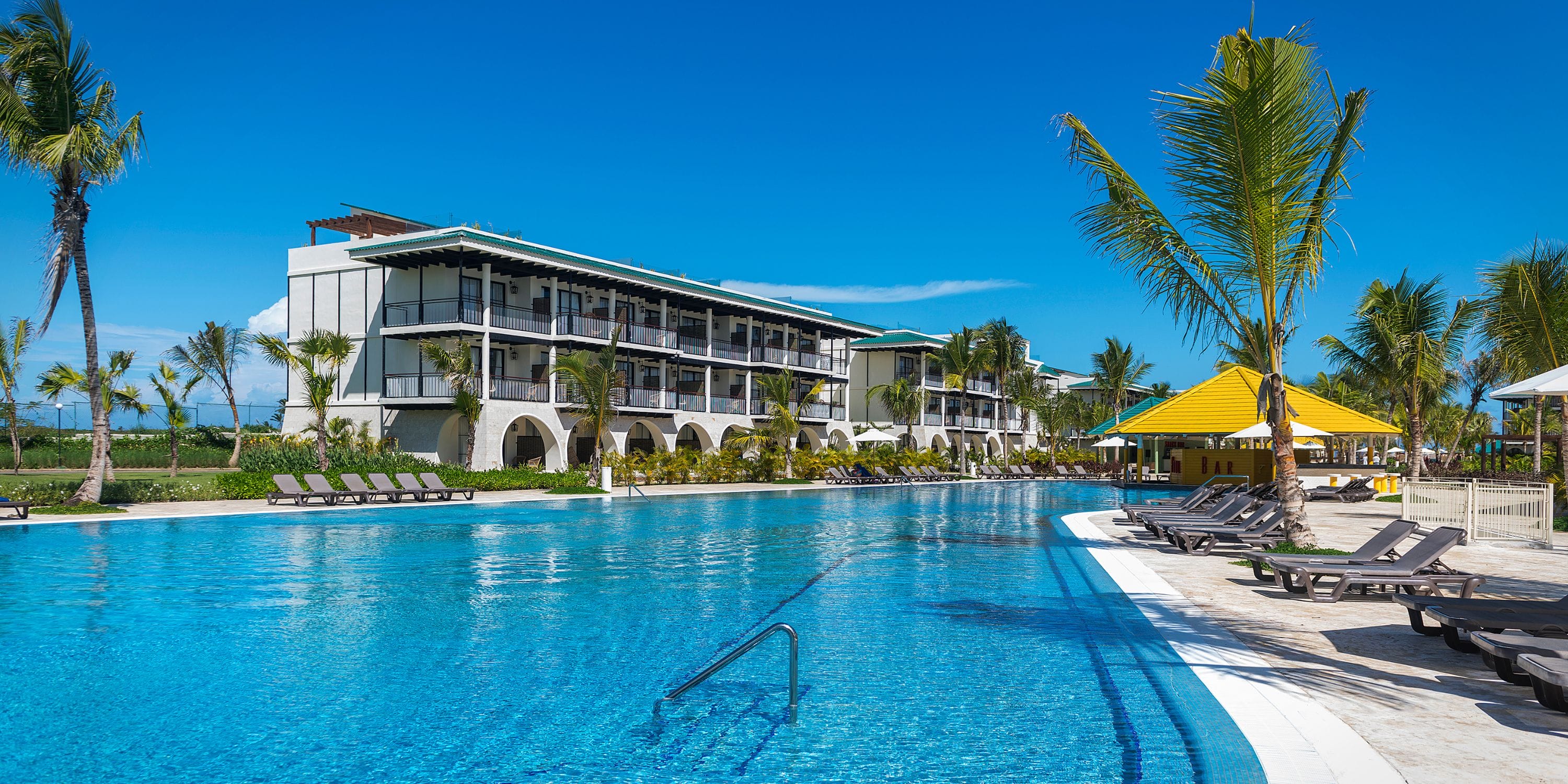 El Beso at Ocean El Faro resort, ideal for a destination wedding, features a pool, palms, and clear skies.