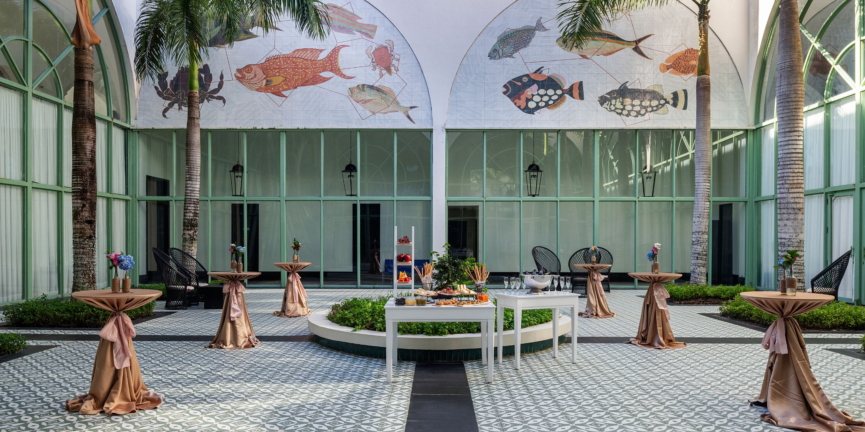 Outdoor courtyard at El Beso, ideal for a destination wedding, with cocktail tables, buffet, palms, and fish murals.