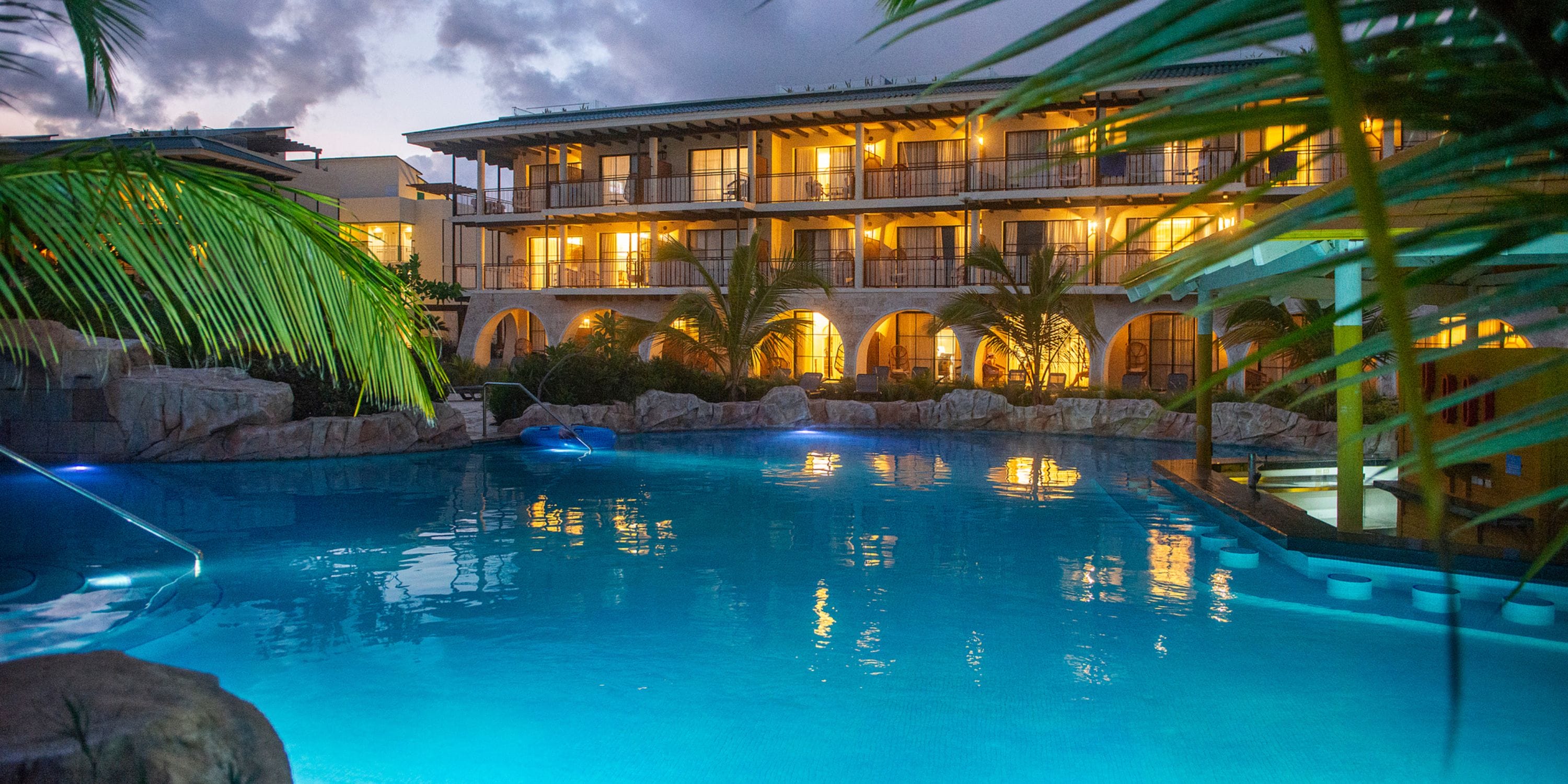 El Beso at Ocean El Faro hotel, perfect for a destination wedding, glows at dusk by a large pool.