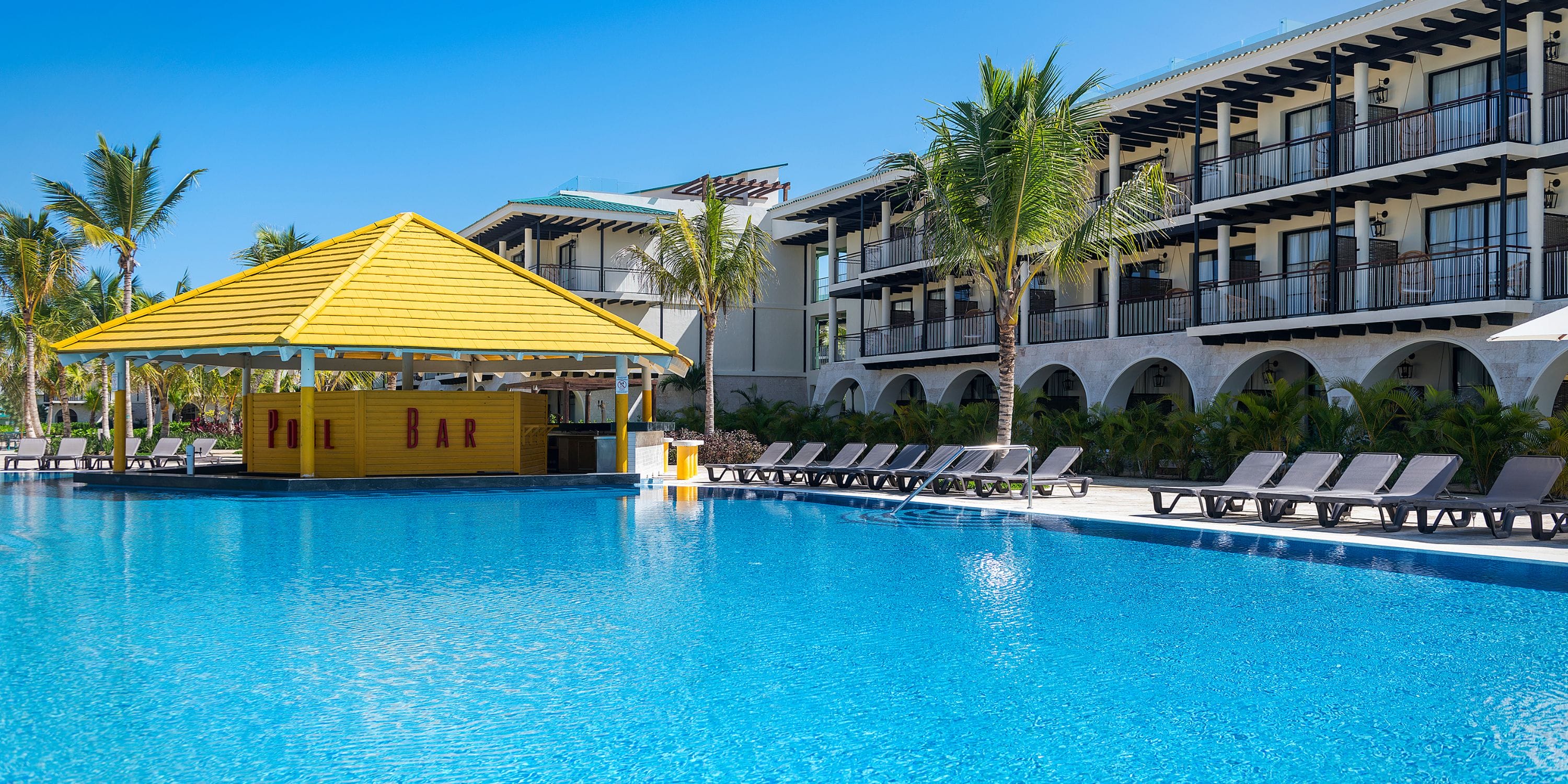 Spacious pool with lounge chairs, yellow bar, and palm trees—ideal for a destination wedding at El Beso.