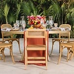 Round outdoor table for six with wooden chairs, floral centerpiece, glassware—destination wedding.