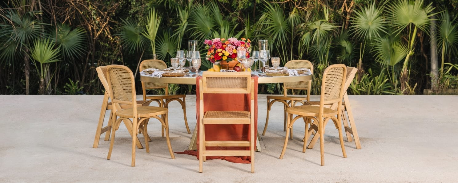 Round outdoor table for six with wooden chairs, floral centerpiece, glassware—destination wedding.