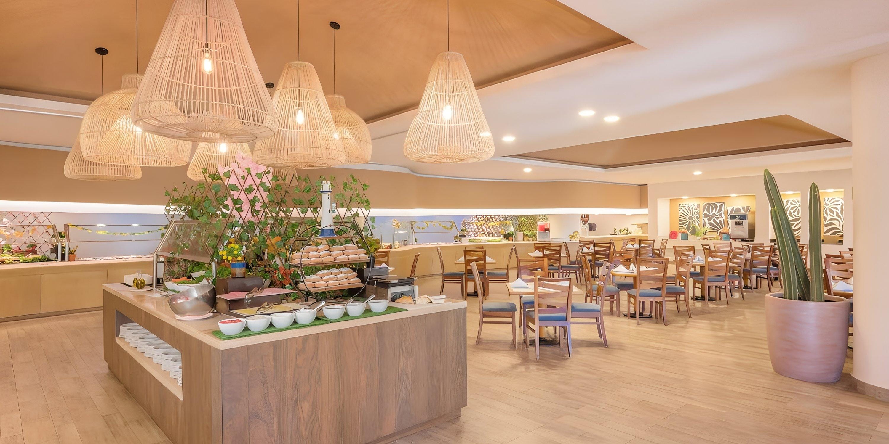Barceló Grand Faro Los Cabos offers a modern buffet, perfect for destination weddings, with wood tables and chairs under stylish hanging lights.