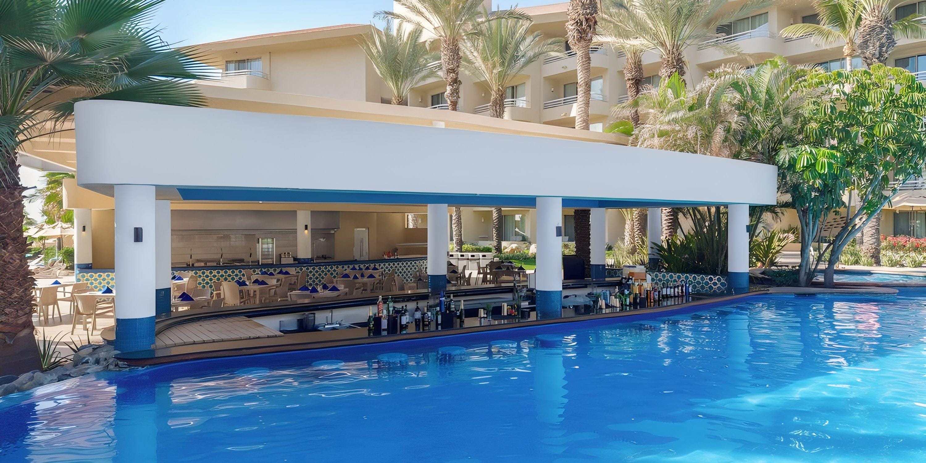 Barceló Grand Faro Los Cabos: Pool swim-up bar, palm trees, hotel—ideal for a destination wedding.