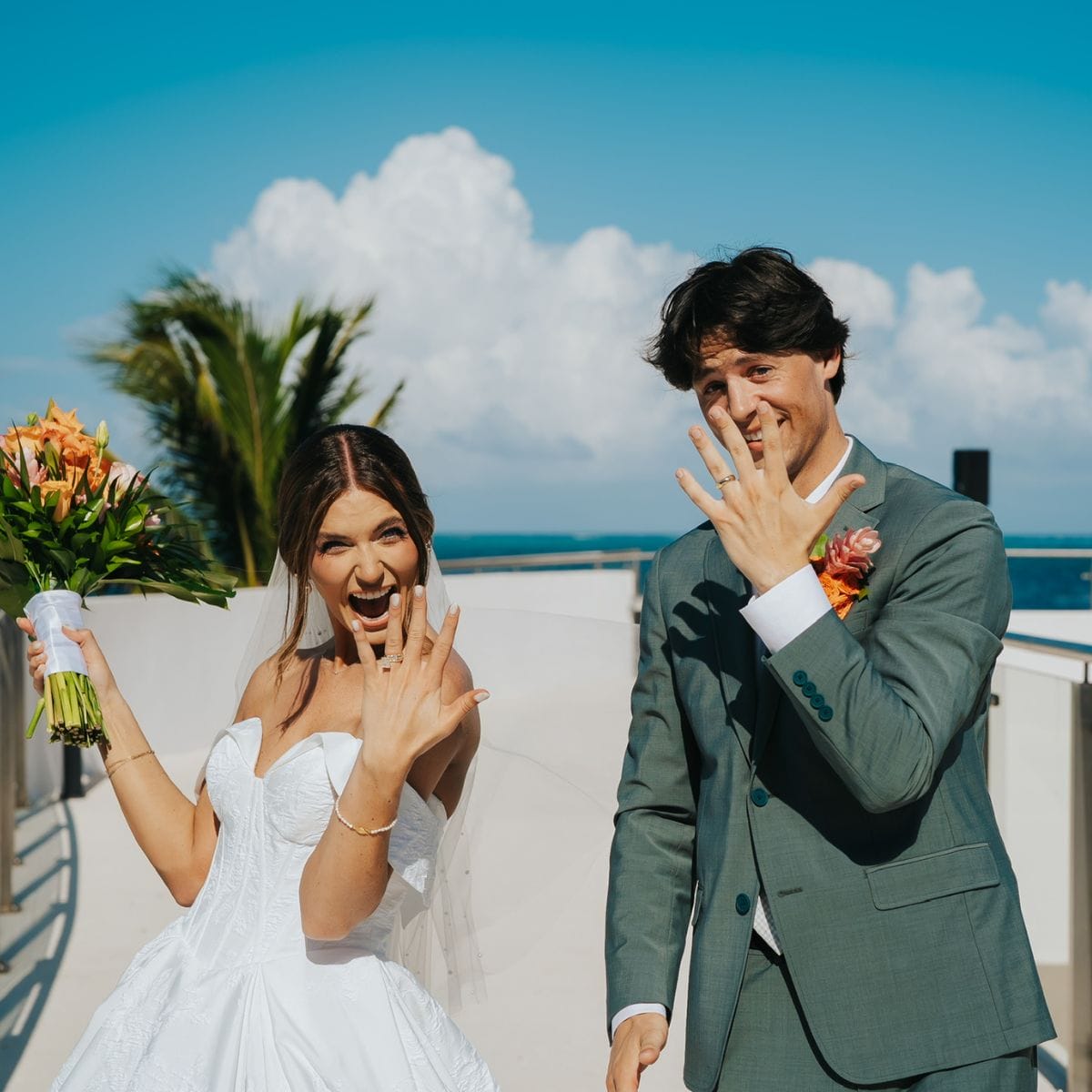 Madison and Blake smile outdoors, proudly displaying wedding rings at their destination wedding.
