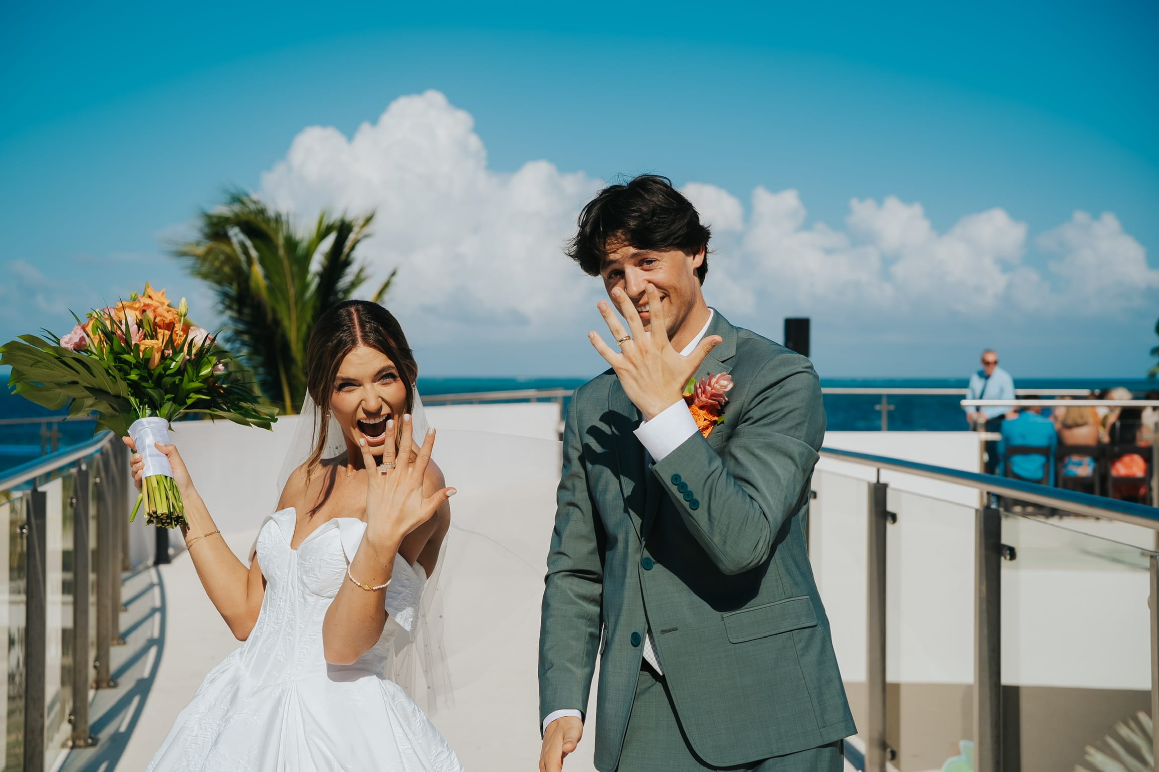 Madison and Blake smile outdoors at their destination wedding, displaying rings on a bright sunny day.