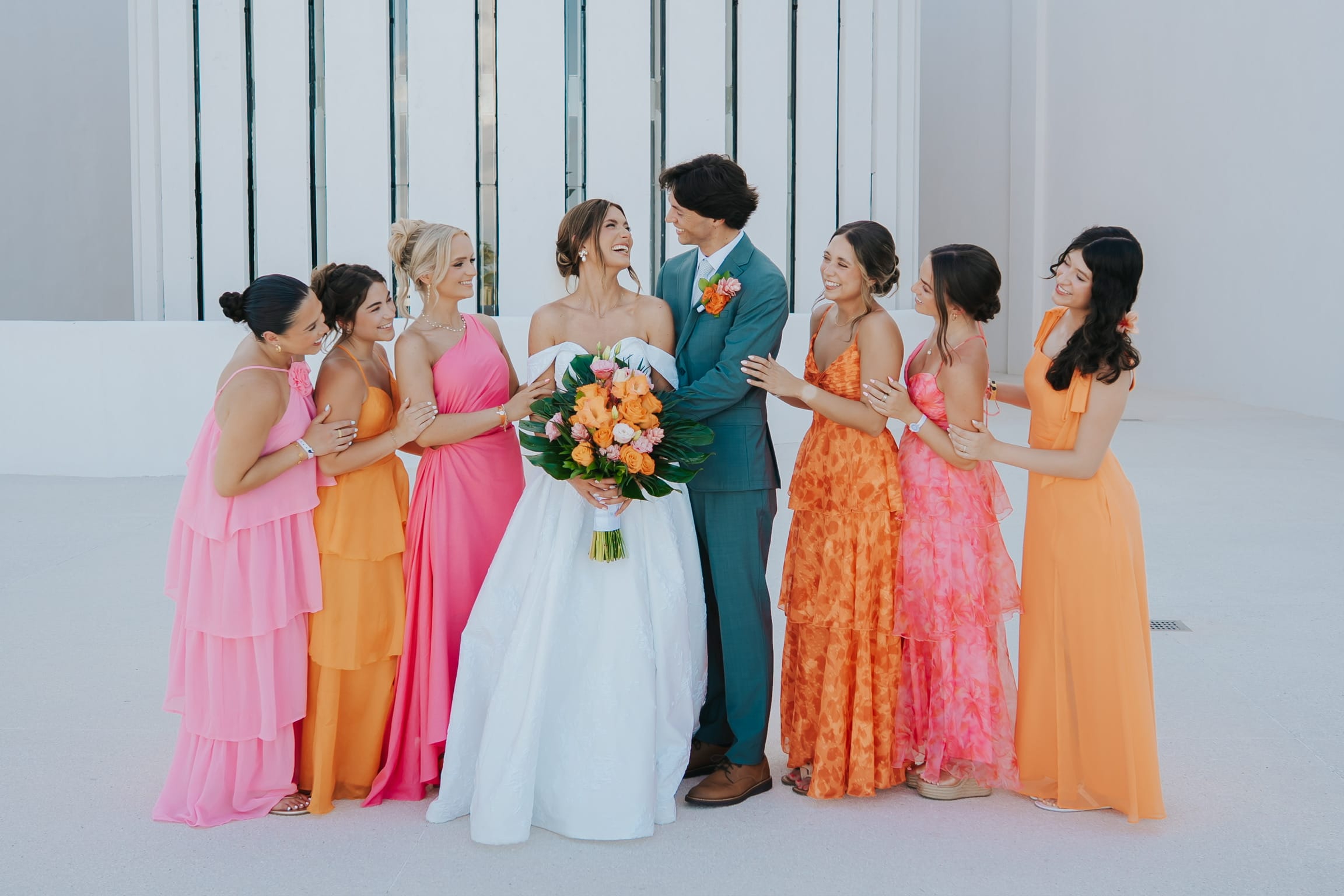 Madison and Blake pose at their destination wedding, surrounded by bridesmaids in pink and orange dresses.