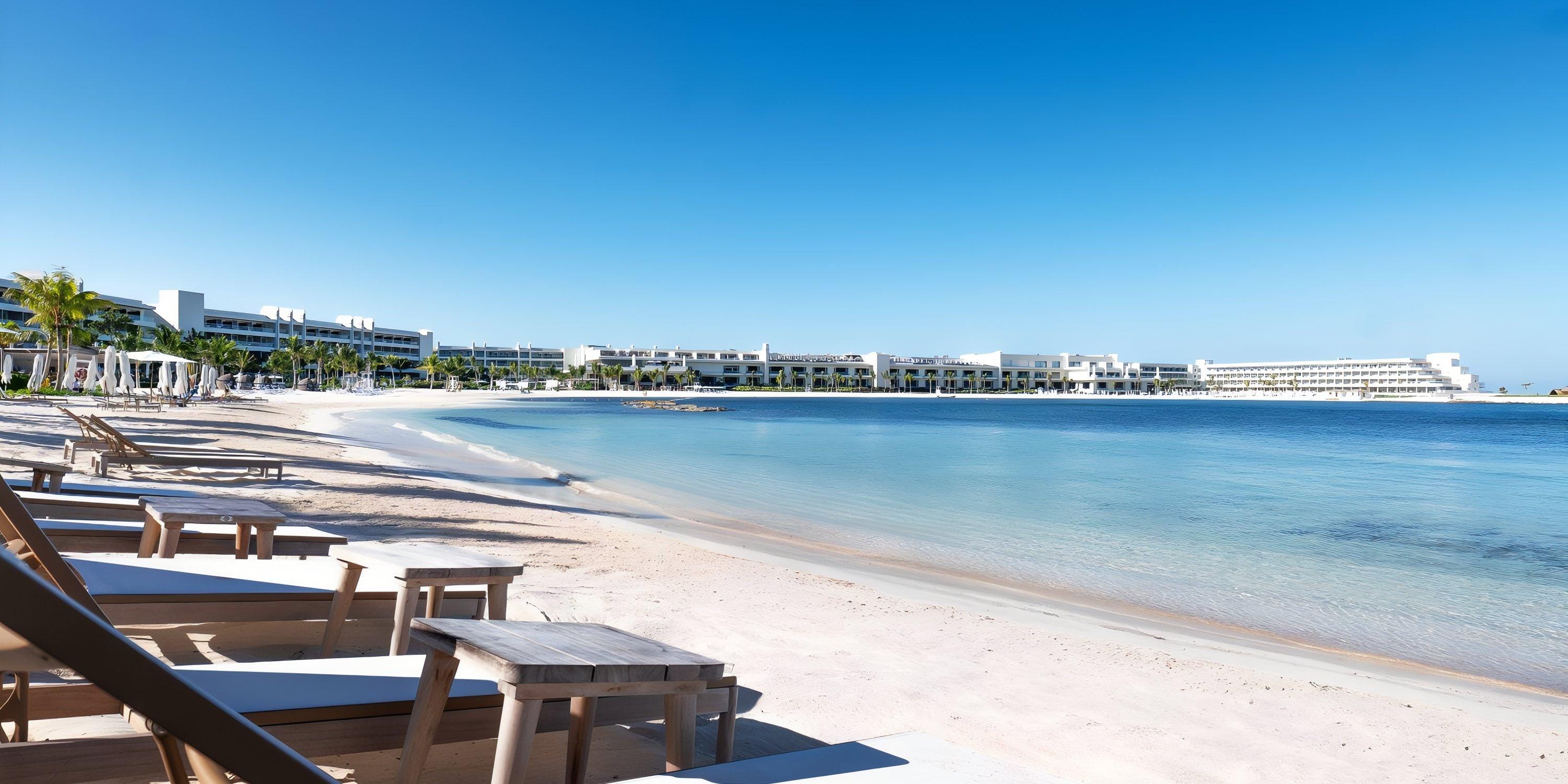 Chairs and tables set up for a destination wedding on the sandy beach at Princess Senses by blue water.