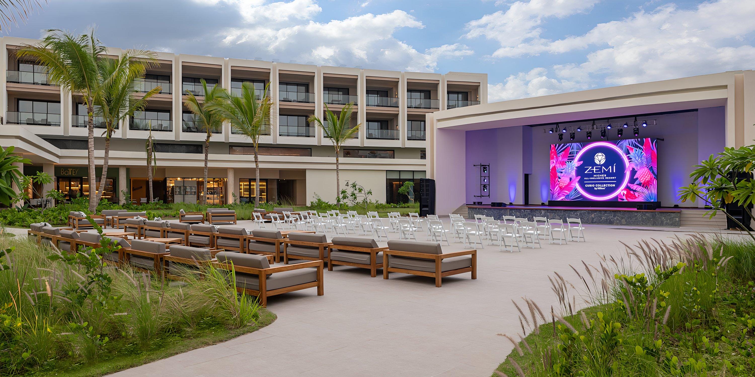 Outdoor wedding event stage with seating set up in front of Hilton Cancun Mar Caribe under a blue sky.