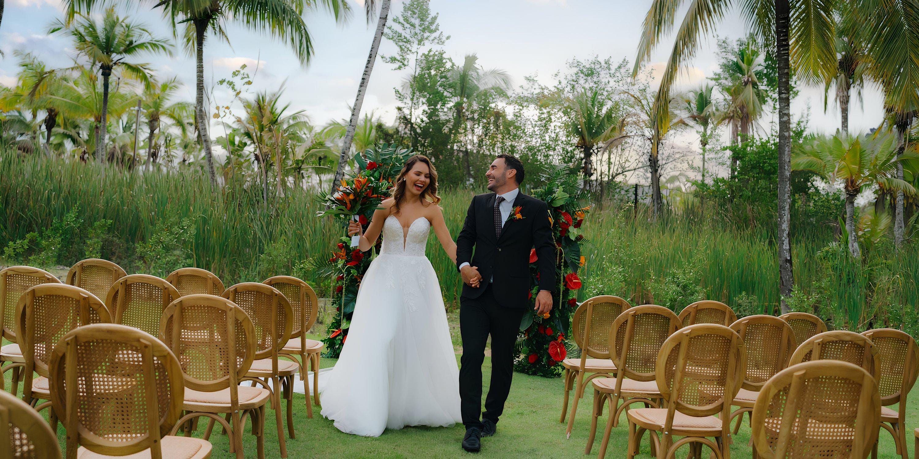 The bride and groom walk down the aisle during their destination wedding at Hilton Cancun Mar Caribe, among palm trees.