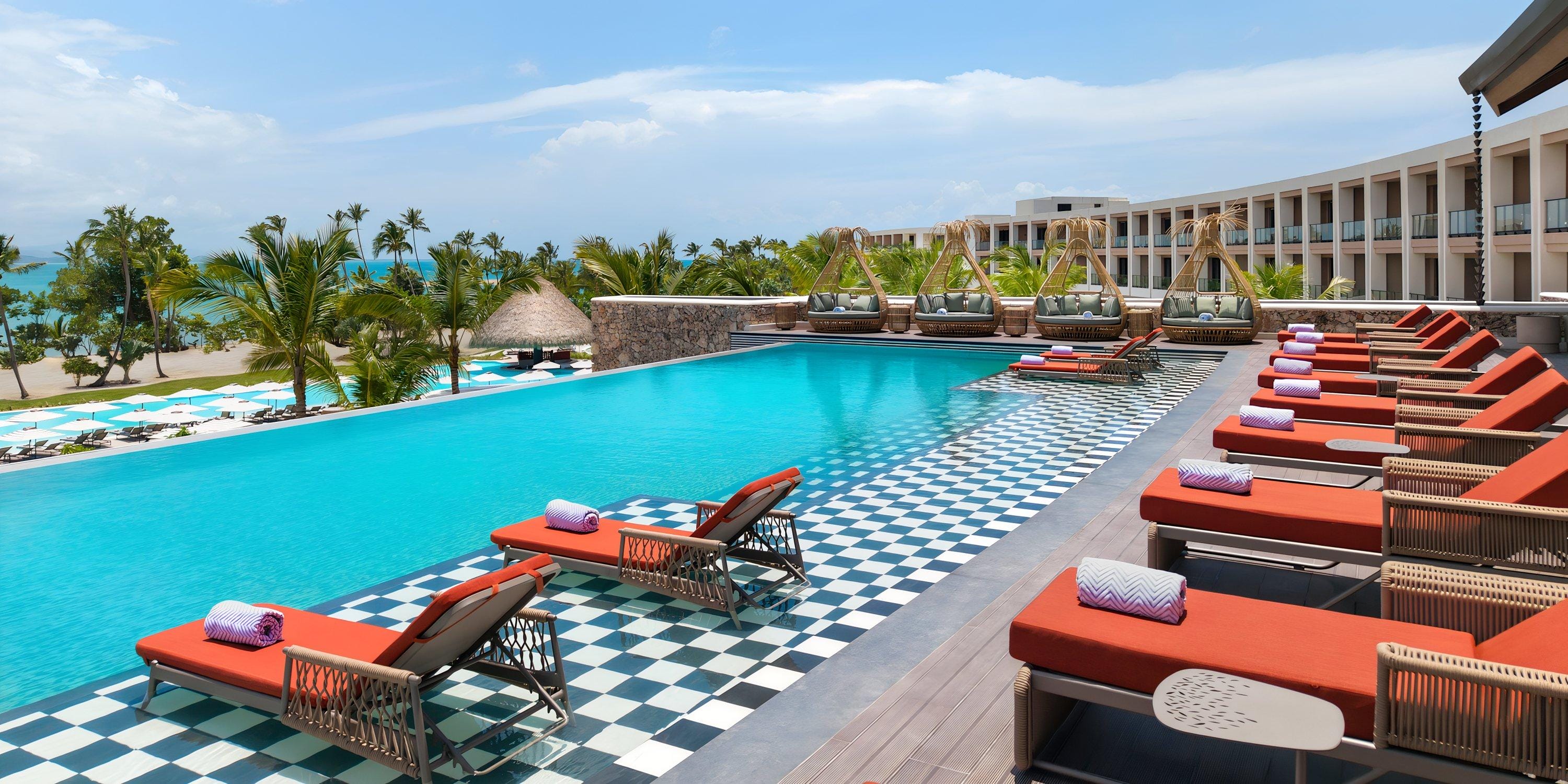 Hilton Cancun Mar Caribe: outdoor pool with red lounge chairs, cabanas, ocean views—ideal for weddings.
