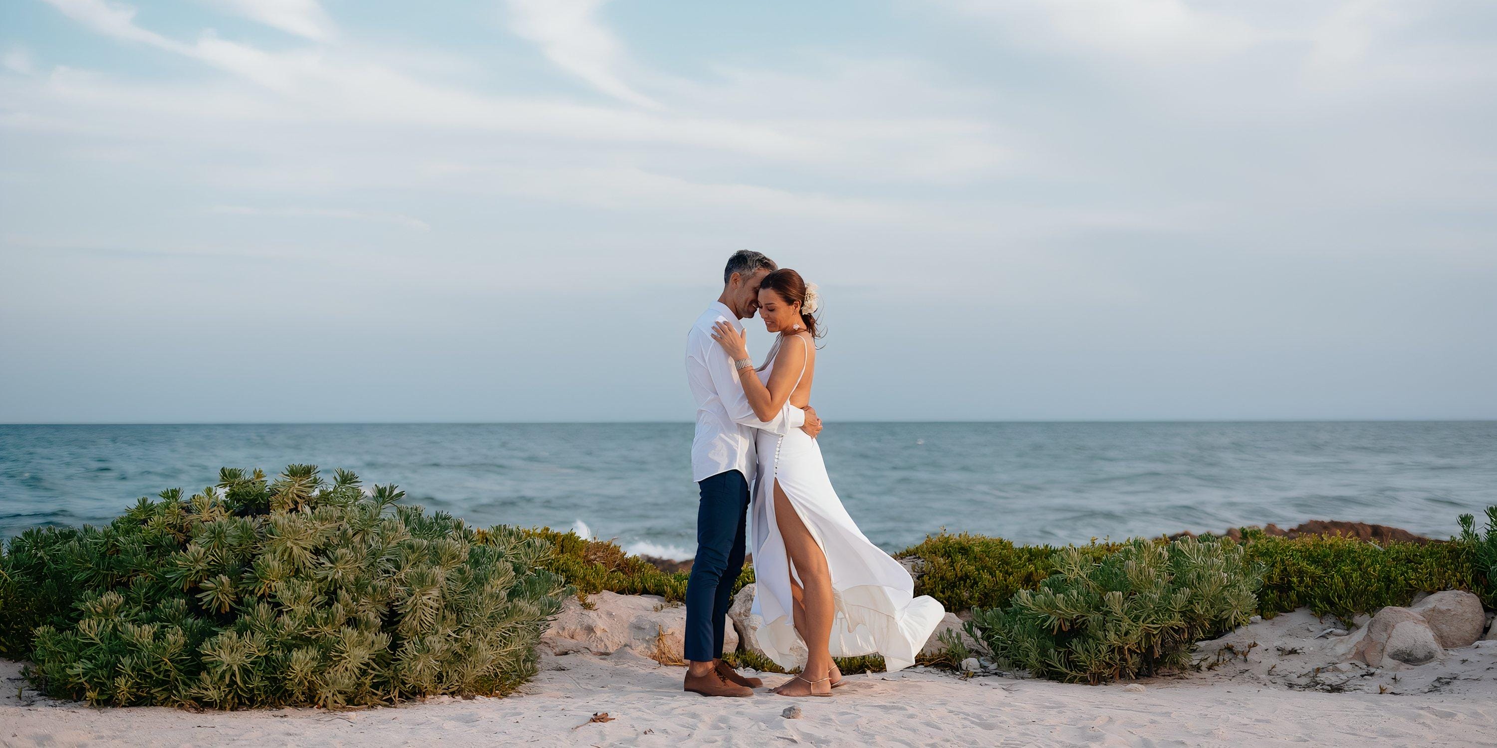 A couple in white embraces on the beach at Hilton Cancun Mar Caribe during their destination wedding.
